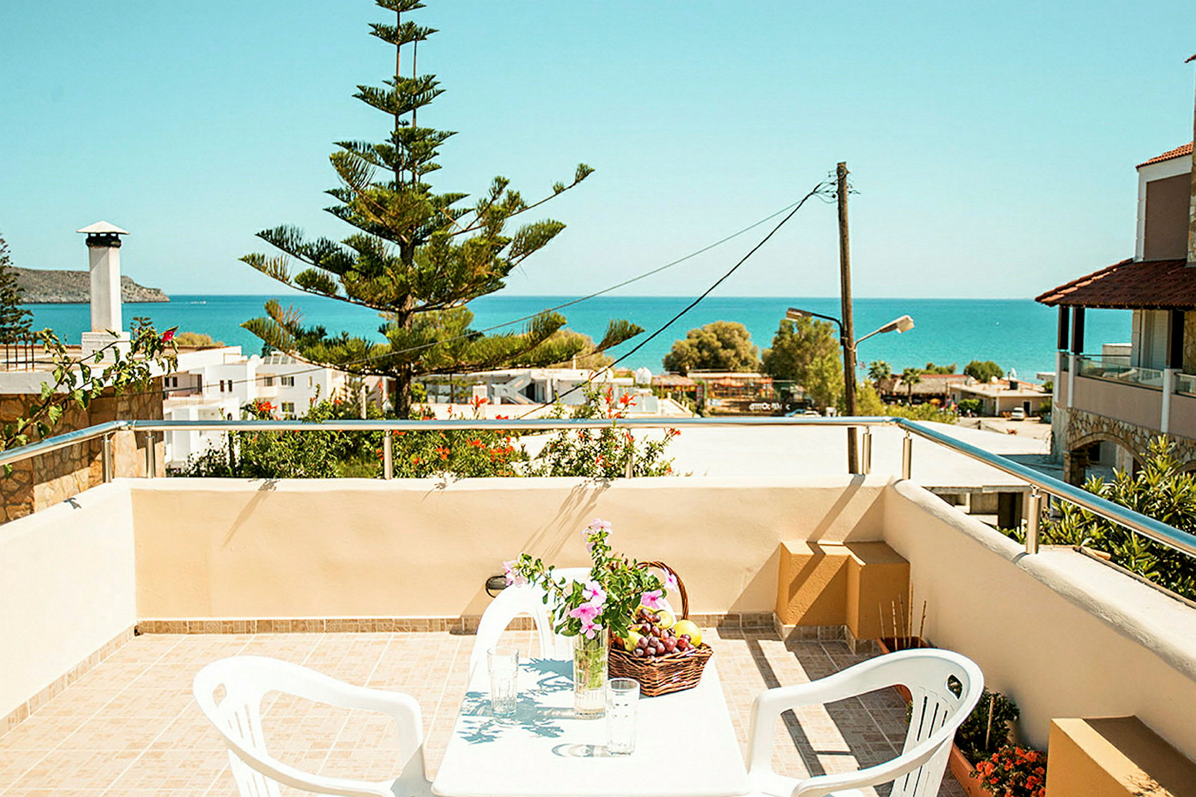 Utsikt från en terrass med bord, stolar och blommor, mot havet. (AI-genererad text)