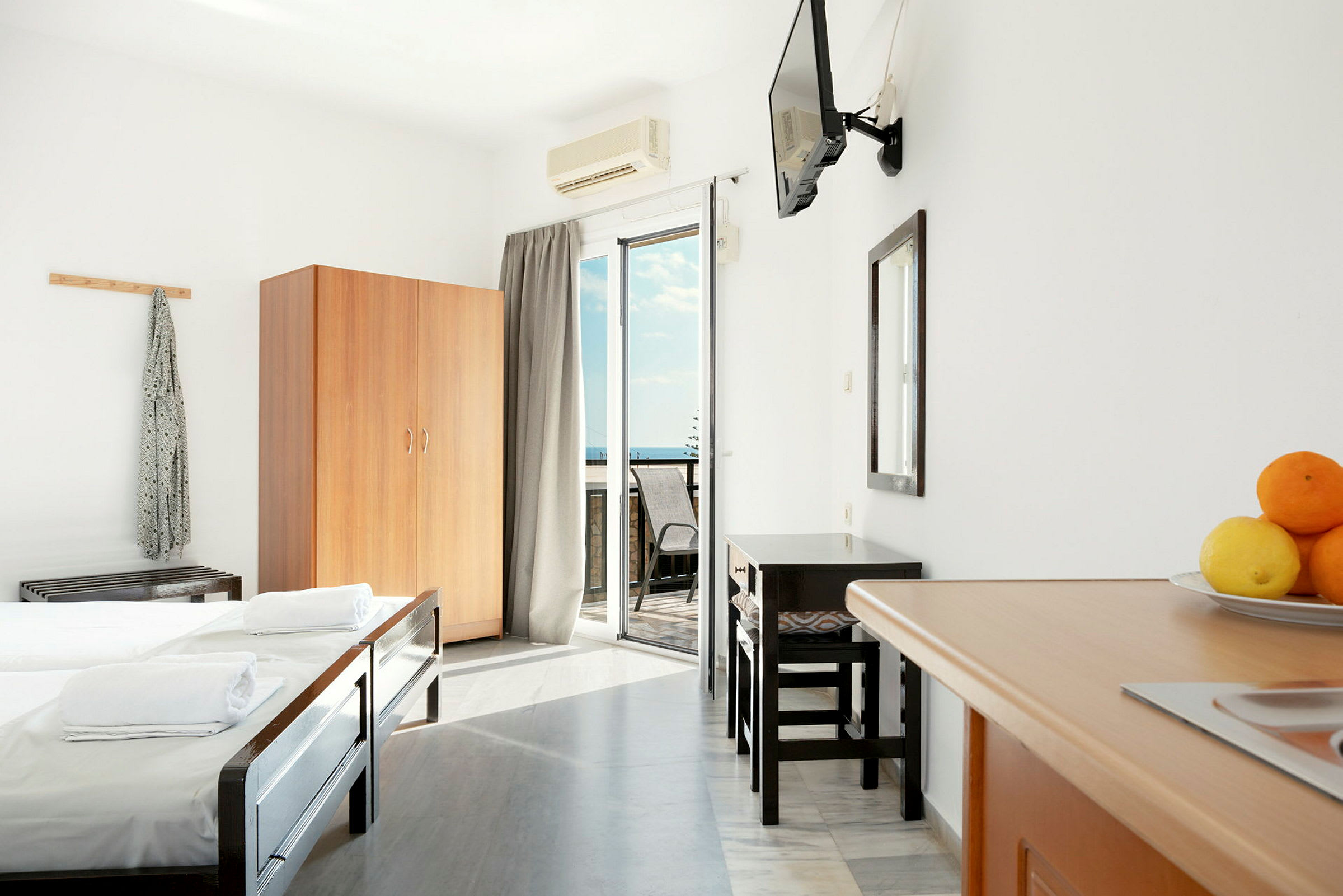 Ett hotellrum med sängar, garderob, tv, spegel, balkong och bord med stolar. (AI-genererad text)