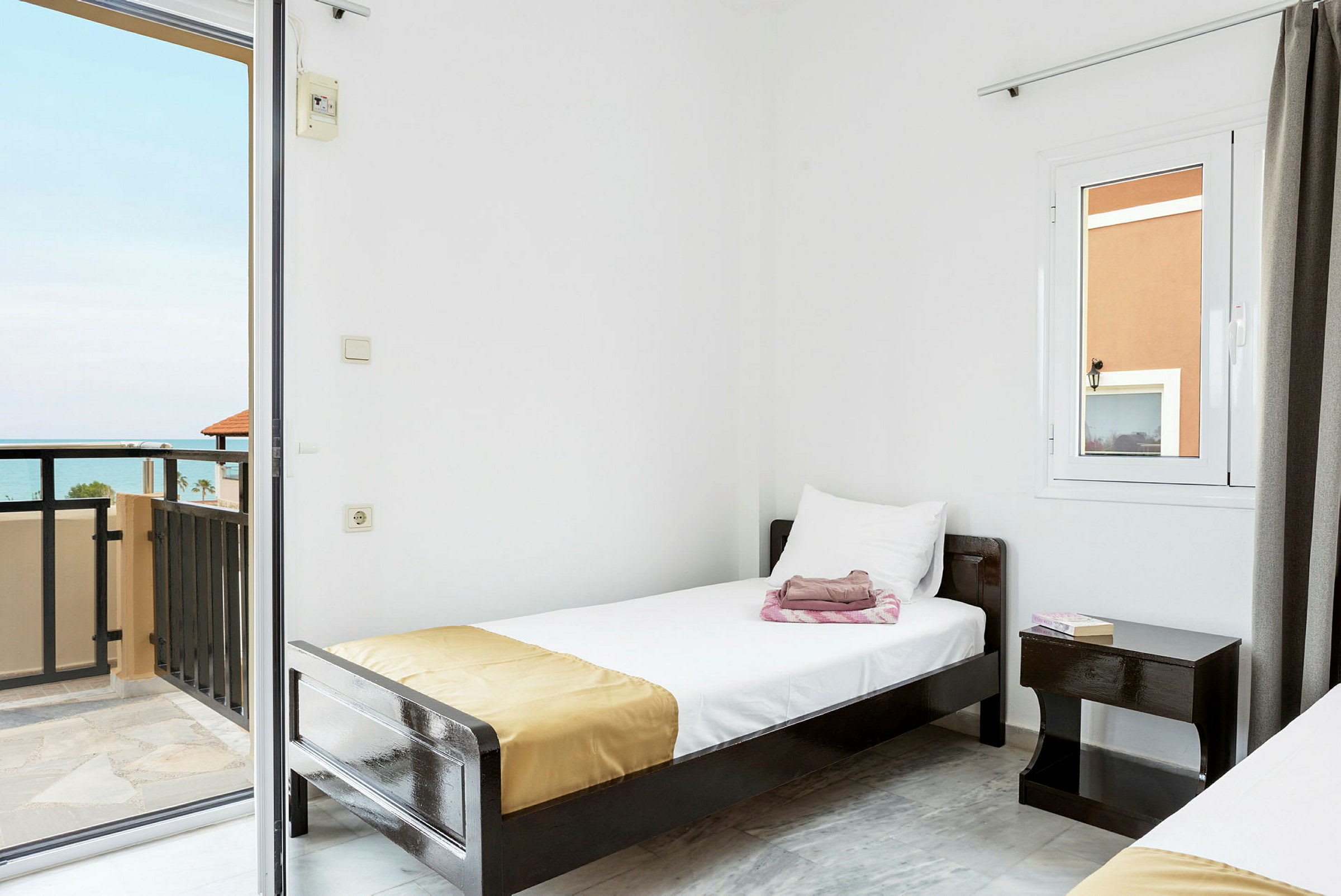 Ett hotellrum med vita väggar, en enkelsäng och en balkong med havsutsikt. (AI-genererad text)
