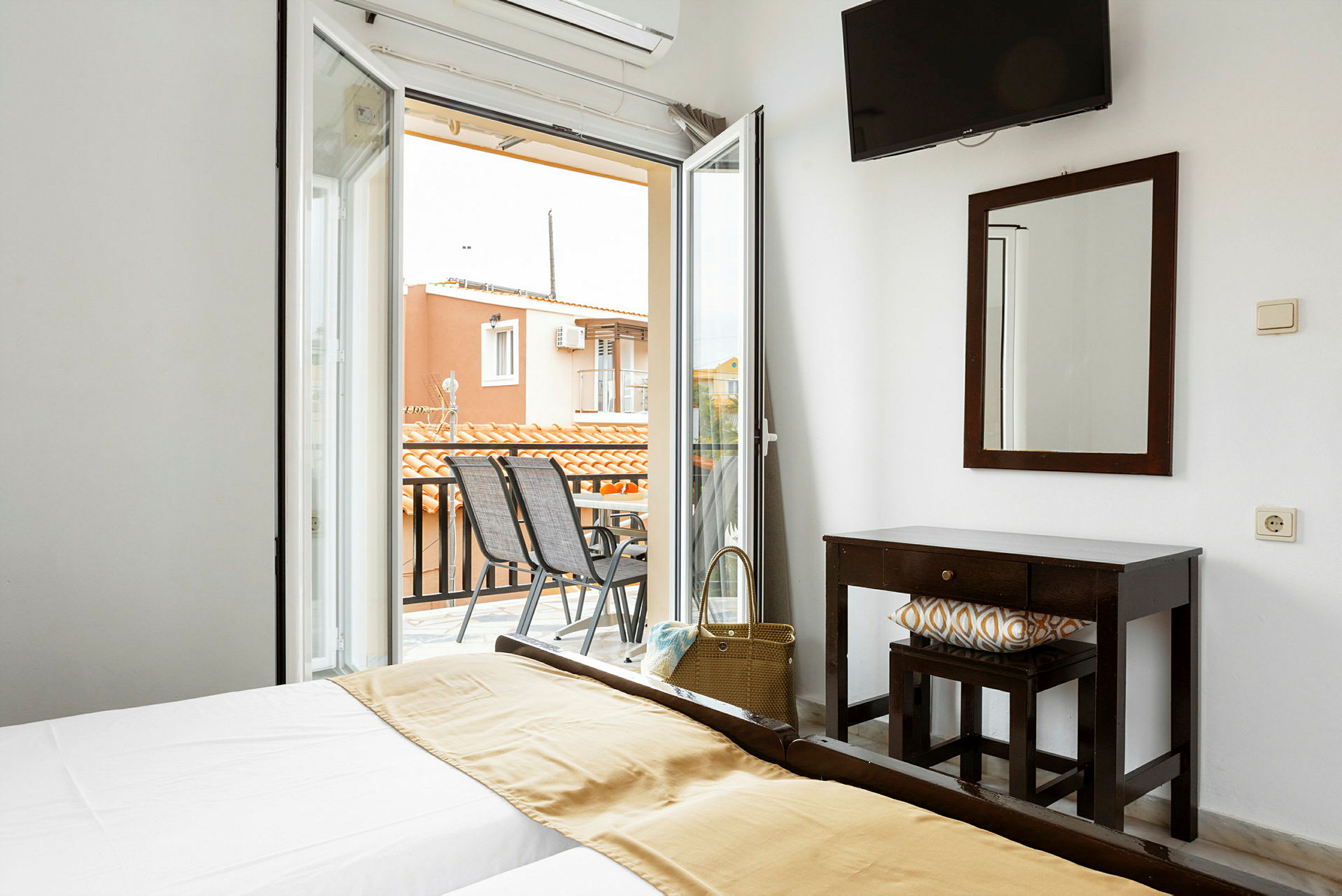 Ett hotellrum med en dubbelsäng och en utgång till en balkong med stolar och utsikt över hustak. (AI-genererad text)