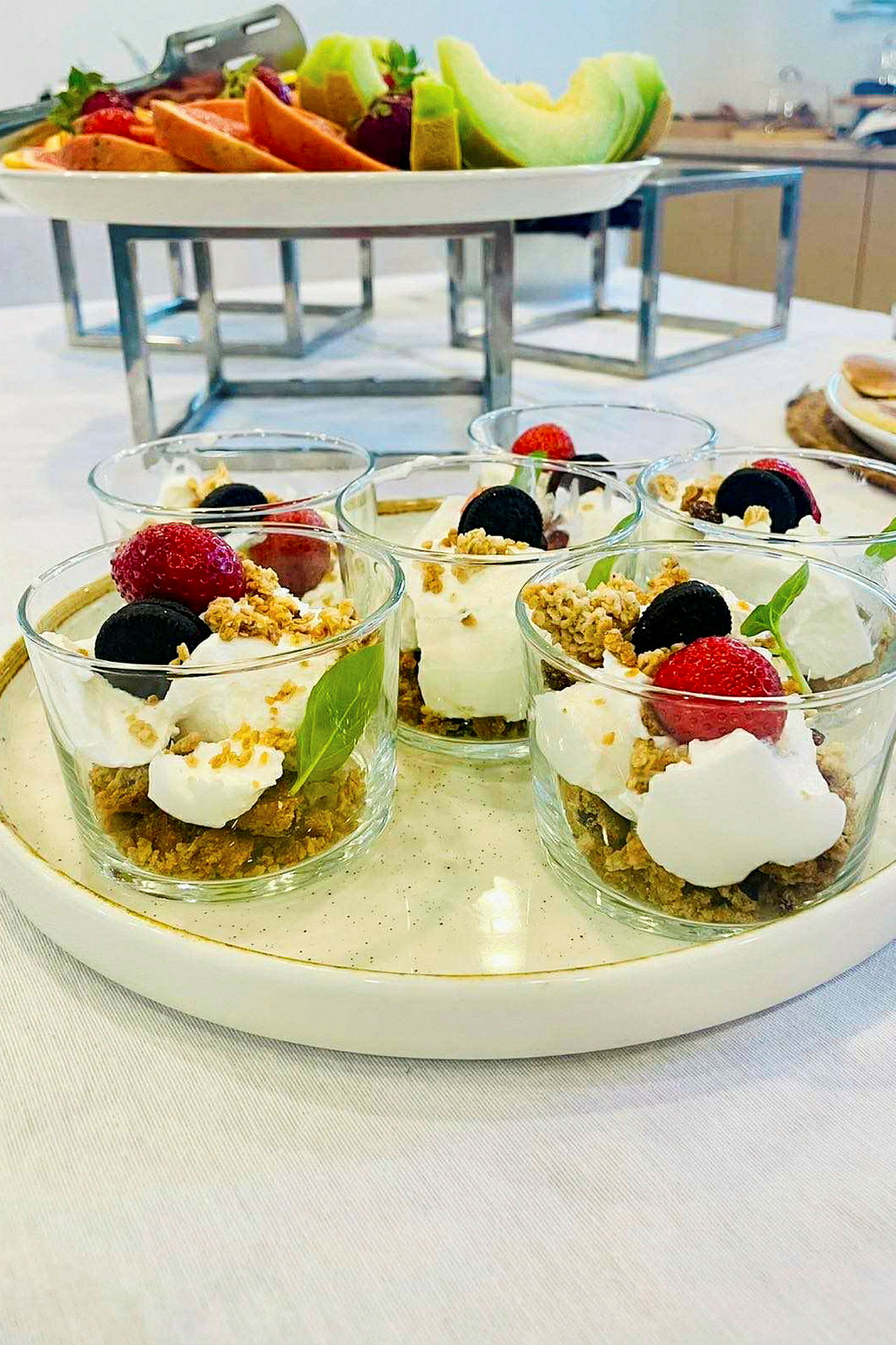 Fyra glas med dessert, dekorerade med färska bär och krispigt topping, på en ljus tallrik. (AI-genererad text)