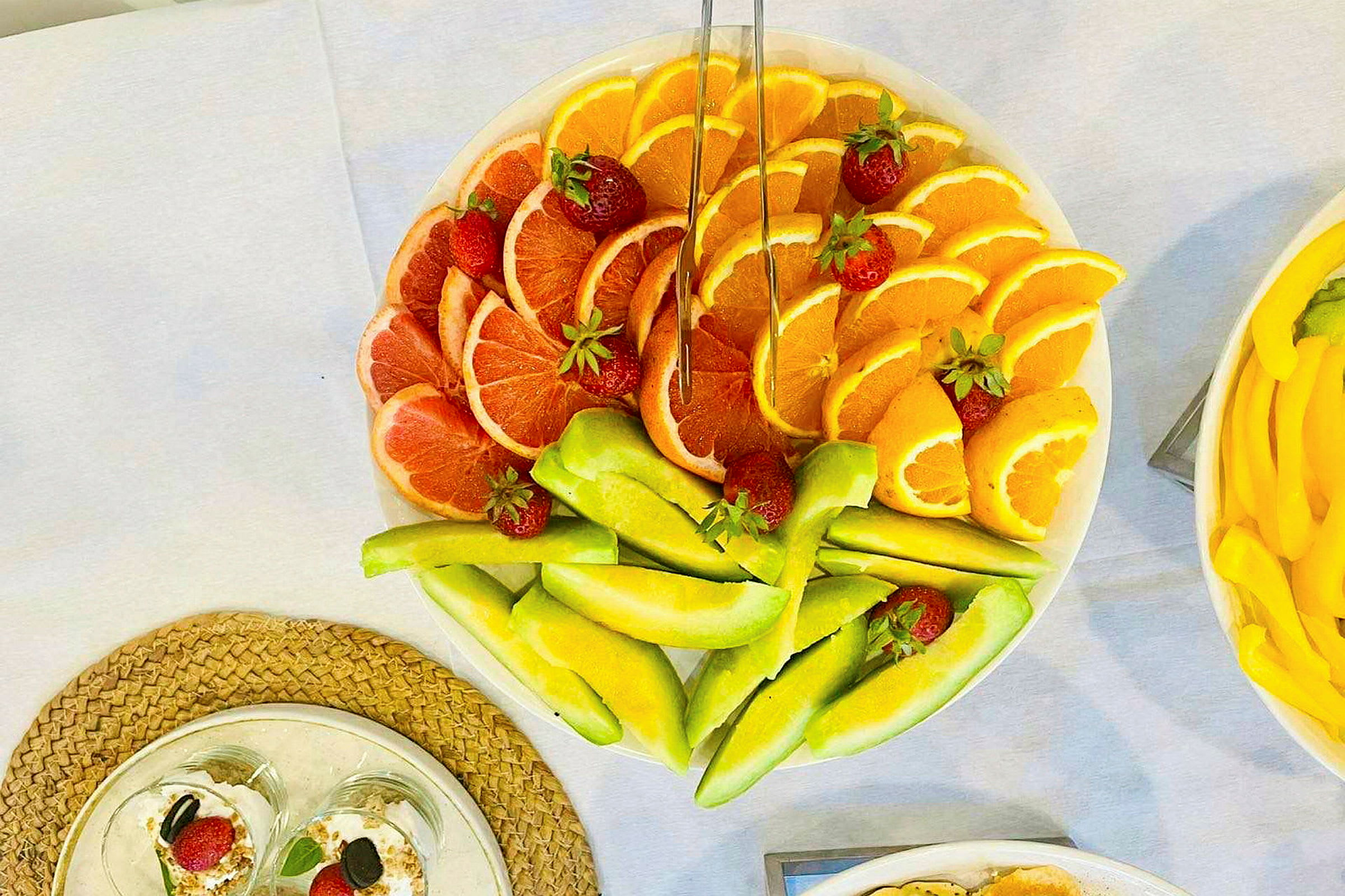 En tallrik med skivad frukt såsom grapefrukt, apelsiner och melon, dekorerad med jordgubbar. (AI-genererad text)