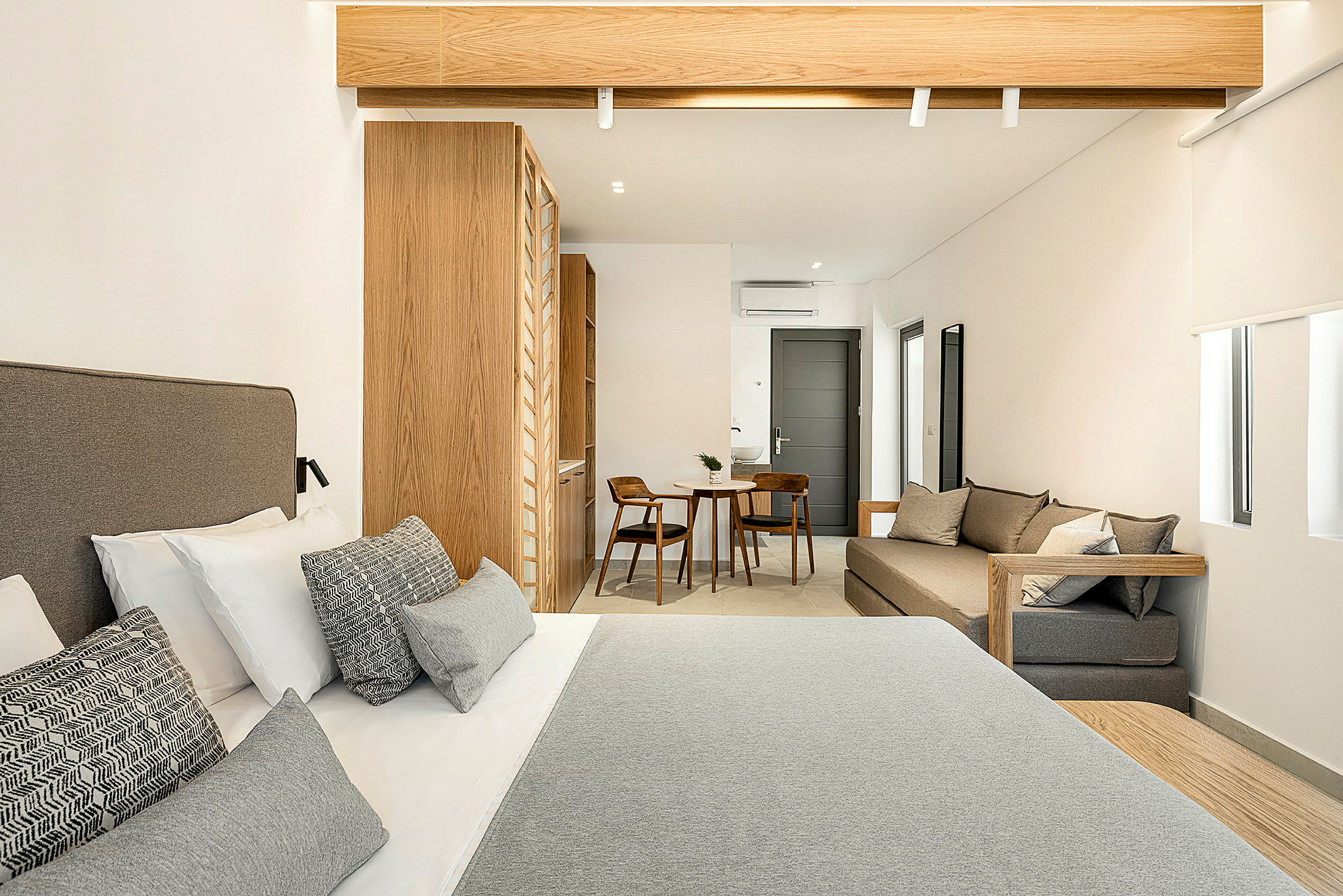 Hotellrum med en dubbelsäng i förgrunden, träinredning och ett mindre sittområde med bord och två stolar i bakgrunden. (AI-genererad text)