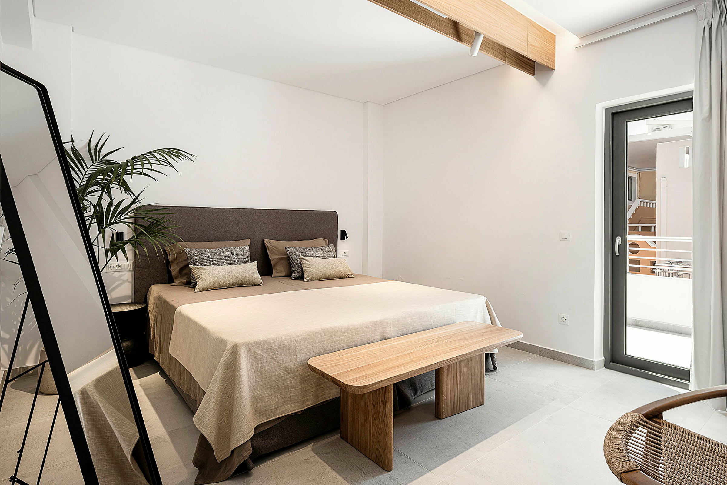 Ett hotellrum med en säng, spegel, växt och ett fönster som vetter mot en balkong. (AI-genererad text)