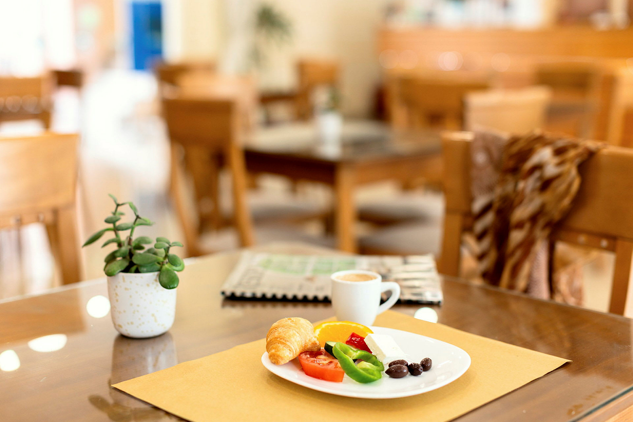 En tallrik serverad med frukost inklusive croissant, grönsaker och kaffe på ett bord med dekorationer. (AI-genererad text)