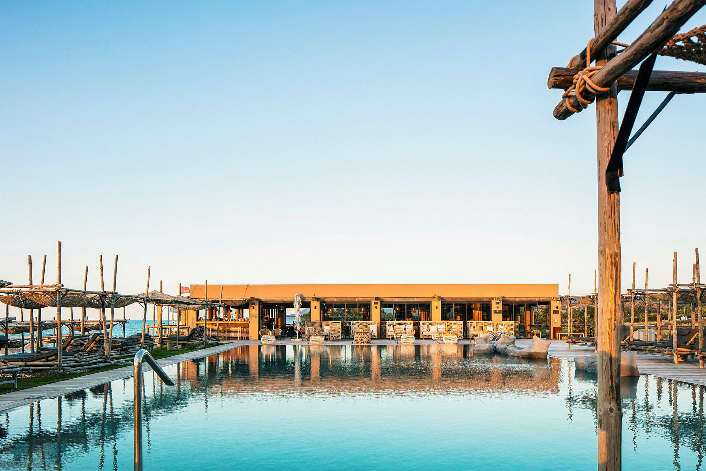 Bild av en pool med solstolar och ett hus i bakgrunden vid soluppgång eller solnedgång. (AI-genererad text)