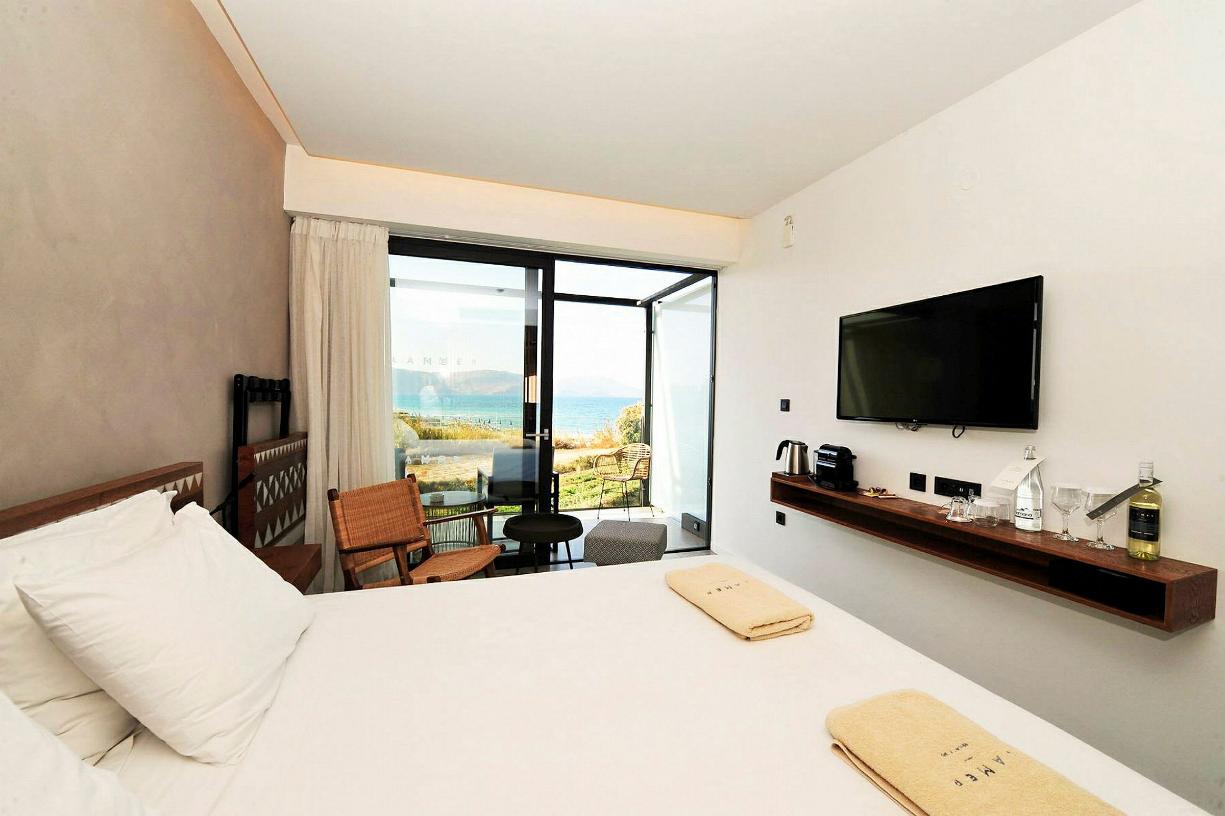Ett hotellrum med en stor säng, en TV på väggen och en utsikt mot havet genom glasdörrar. (AI-genererad text)