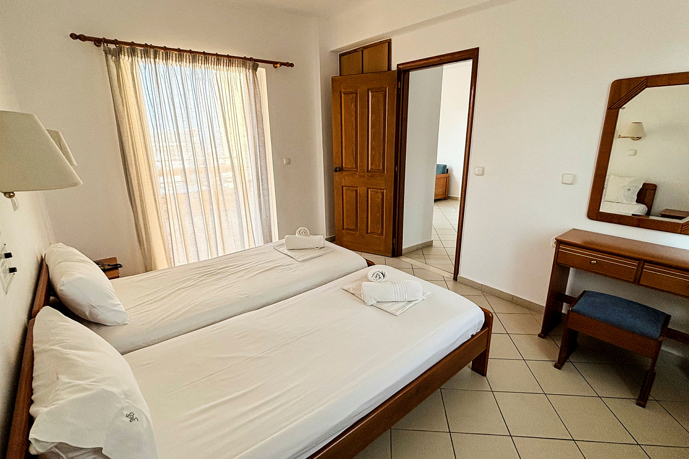 Hotellrum med två enkelsängar, skrivbord och spegel. (AI-genererad text)