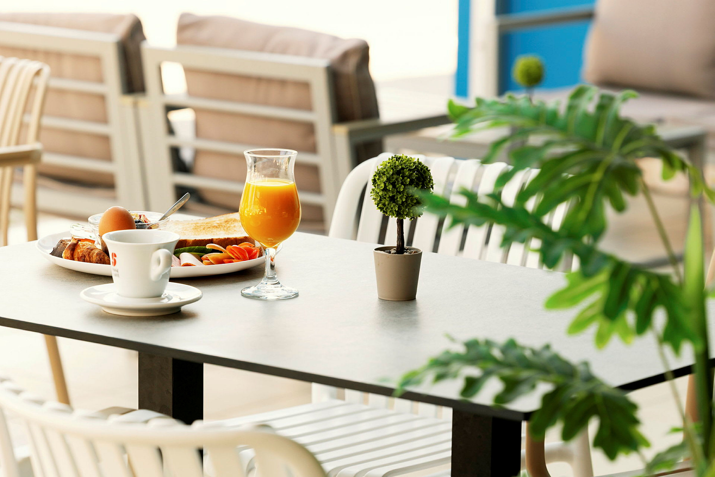 Ett dukat bord med frukost som inkluderar ett glas apelsinjuice, en kaffe, en tallrik med bröd och tillbehör, samt en liten dekorativ grön växt. (AI-genererad text)