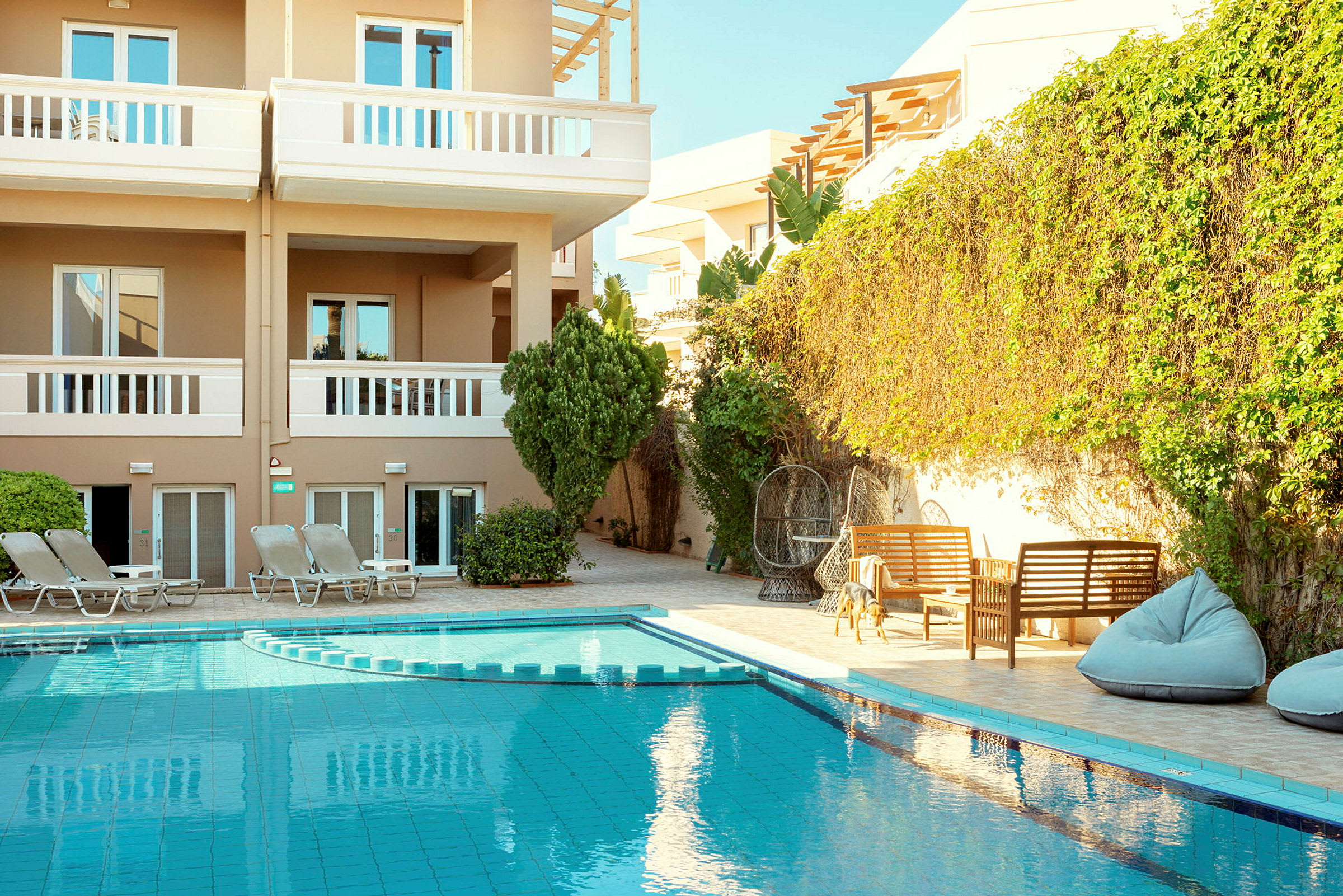 Exteriör av en byggnad med balkonger, pool och omgivande solstolar och sittmöbler. (AI-genererad text)