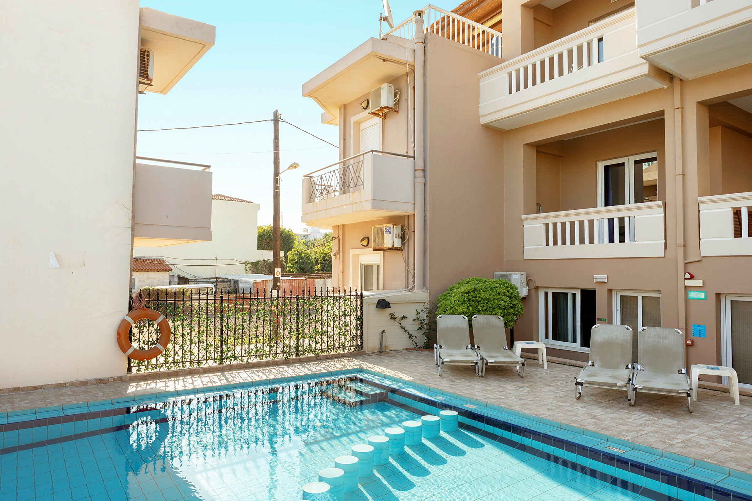 Utomhusområde med pool och solstolar vid sidan av en byggnad. (AI-genererad text)