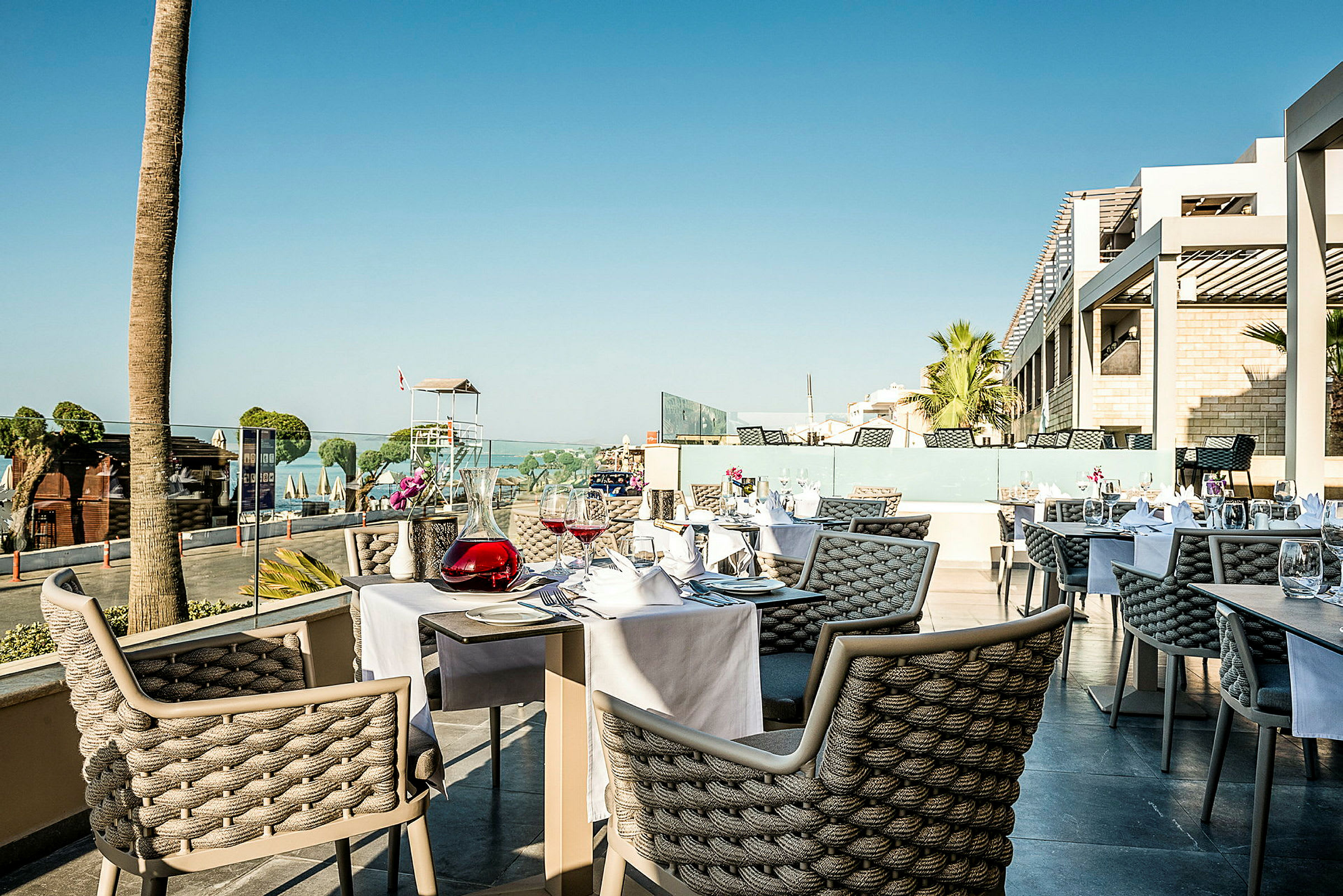 Utomhusrestaurang med dukade bord och utsikt över strand och hav. (AI-genererad text)