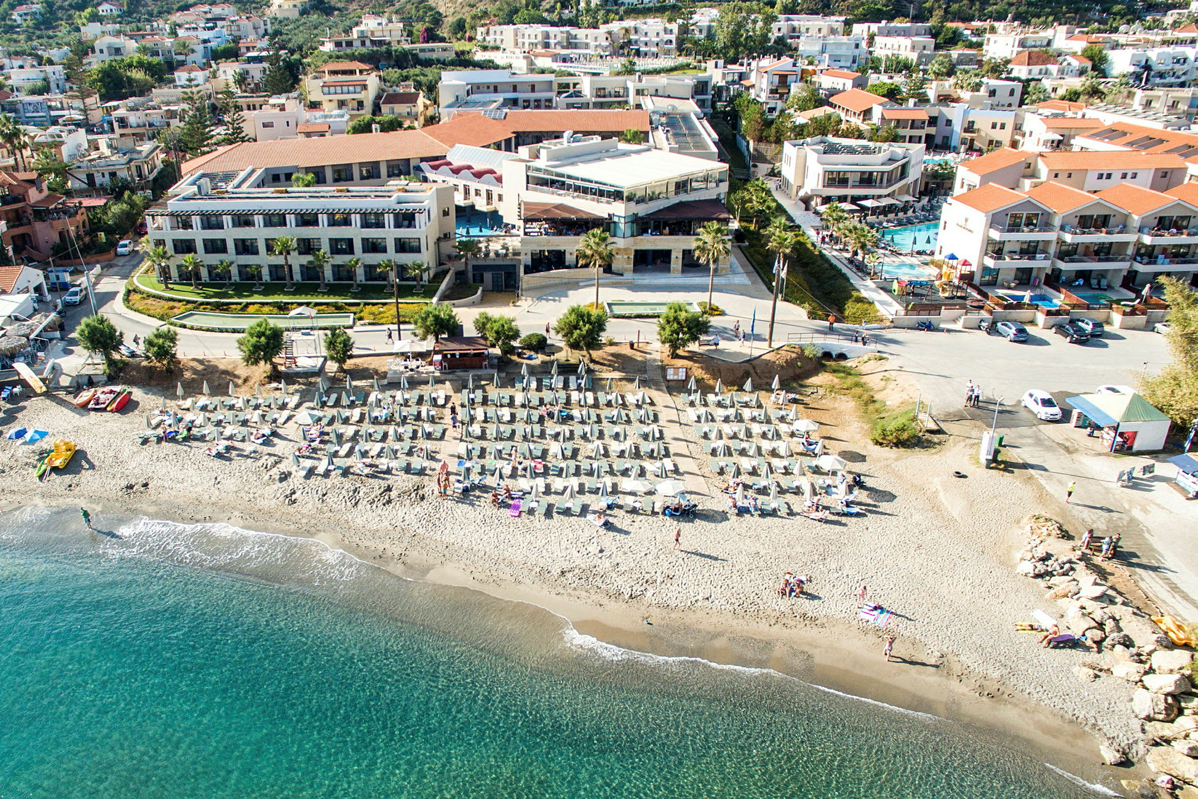 Bild av en strand med solstolar och parasoller, med hotell och byggnader i bakgrunden. (AI-genererad text)