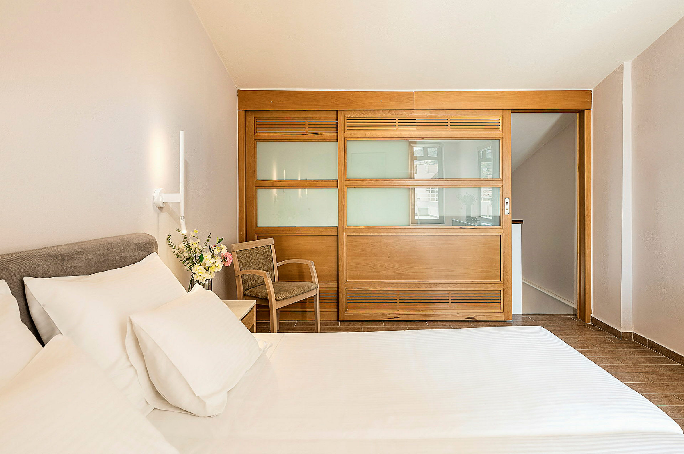 Hotellrum med säng, stol och en träpanel med glas. (AI-genererad text)