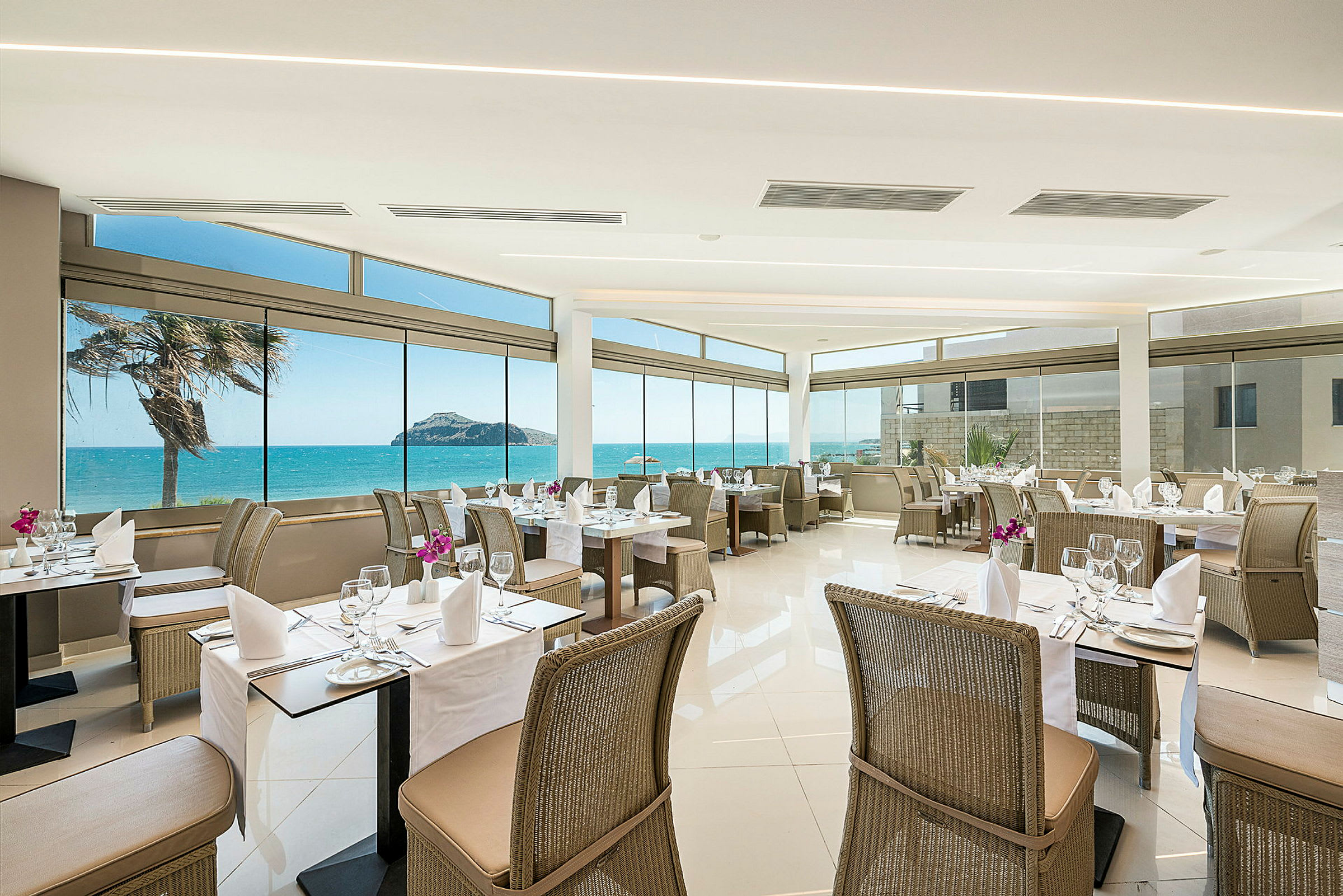 Restaurang med utsikt mot havet, dukade bord och rottingstolar. (AI-genererad text)