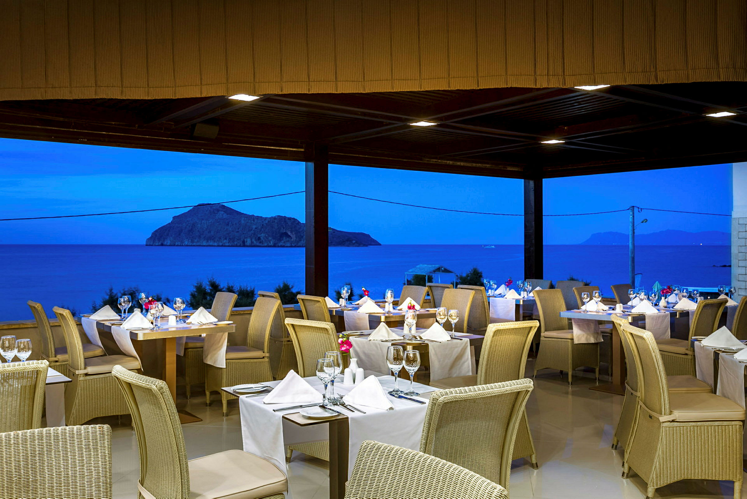 Restaurang med dukade bord och havsutsikt i kvällsljus. (AI-genererad text)