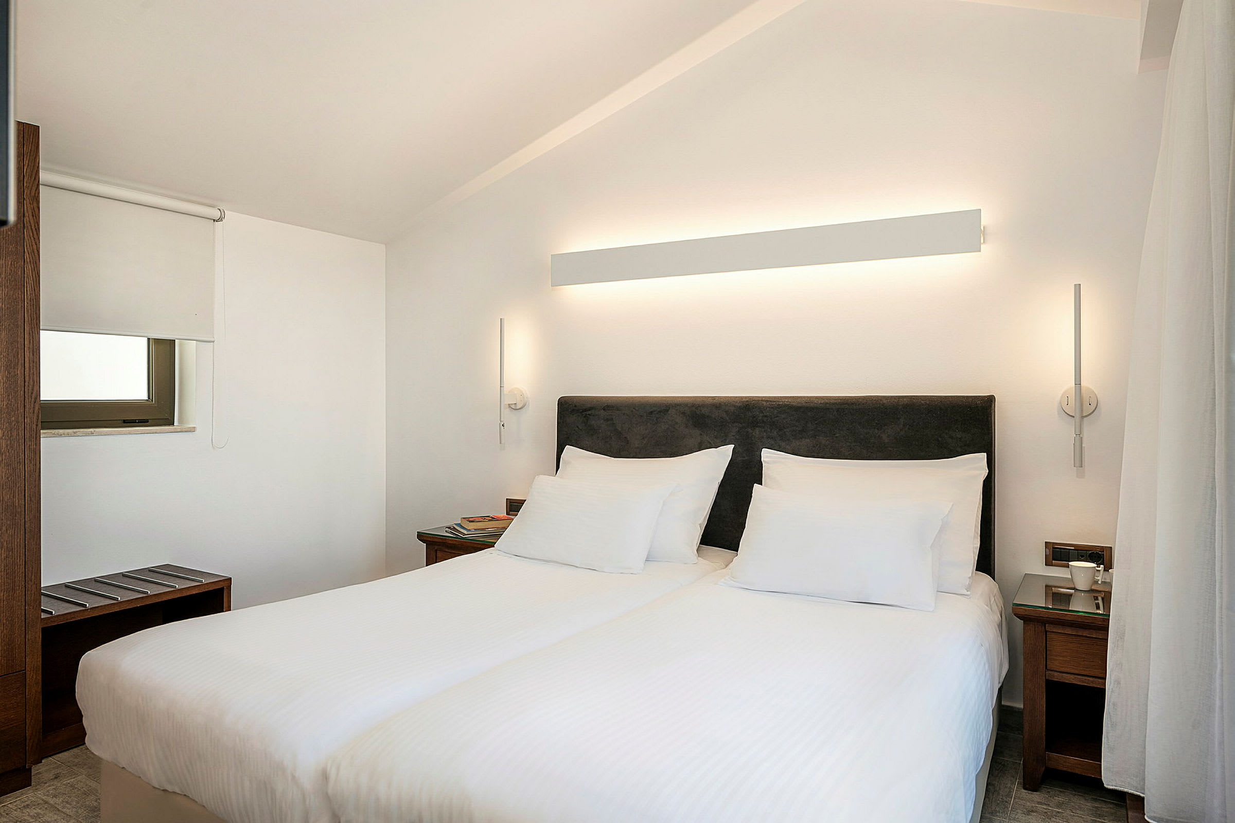 Ett hotellrum med två enkelsängar, vit vägg och modern belysning. (AI-genererad text)