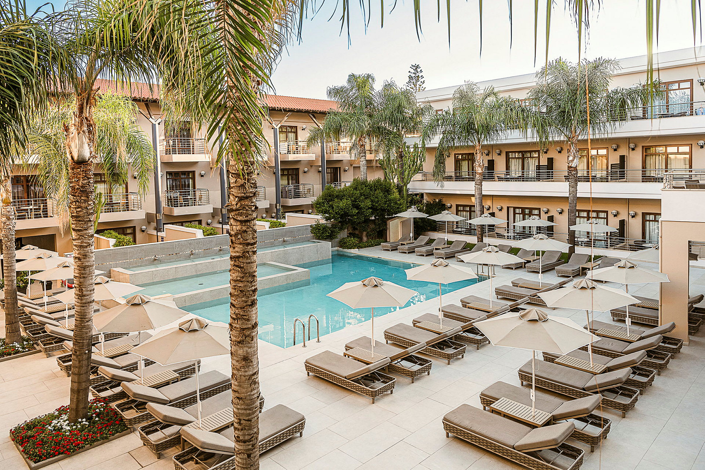 Ett hotellområde med en pool och solstolar omgivna av palmer. (AI-genererad text)