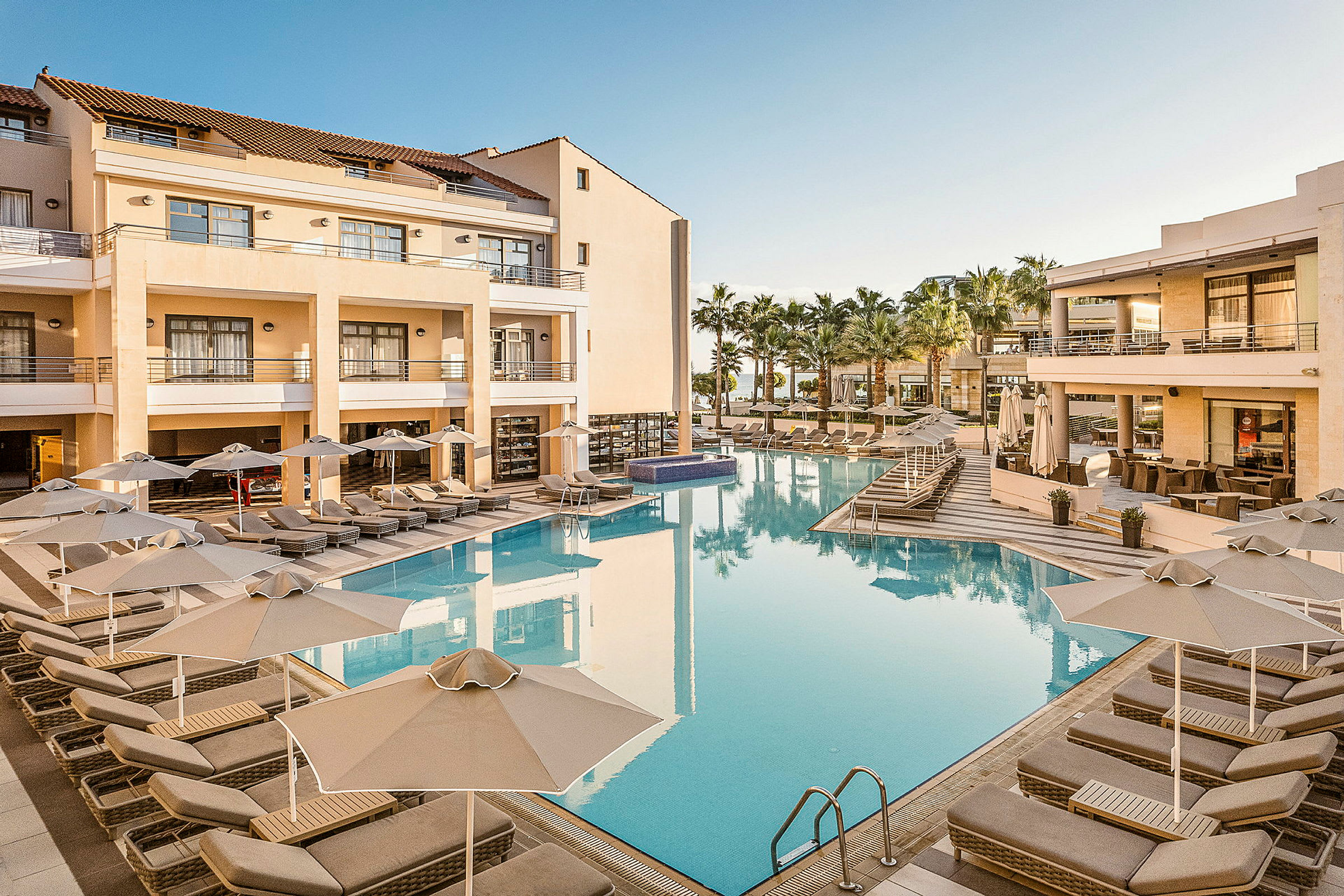 Bild av ett hotellområde med en pool och solstolar, omgivna av byggnader med balkonger och palmer. (AI-genererad text)
