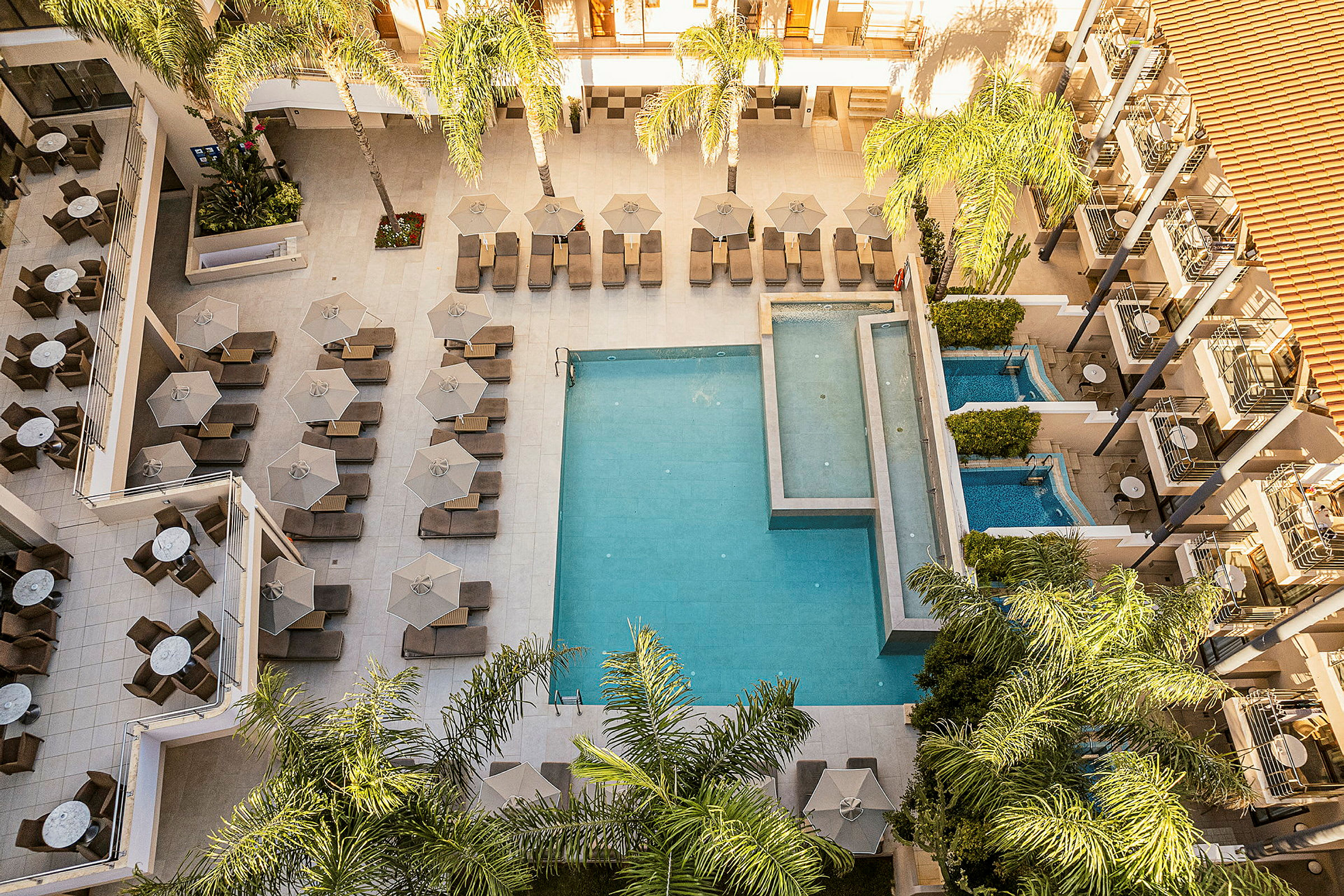 Utsikt över ett hotellområde med pool, solstolar och parasoller omgivna av palmer. (AI-genererad text)