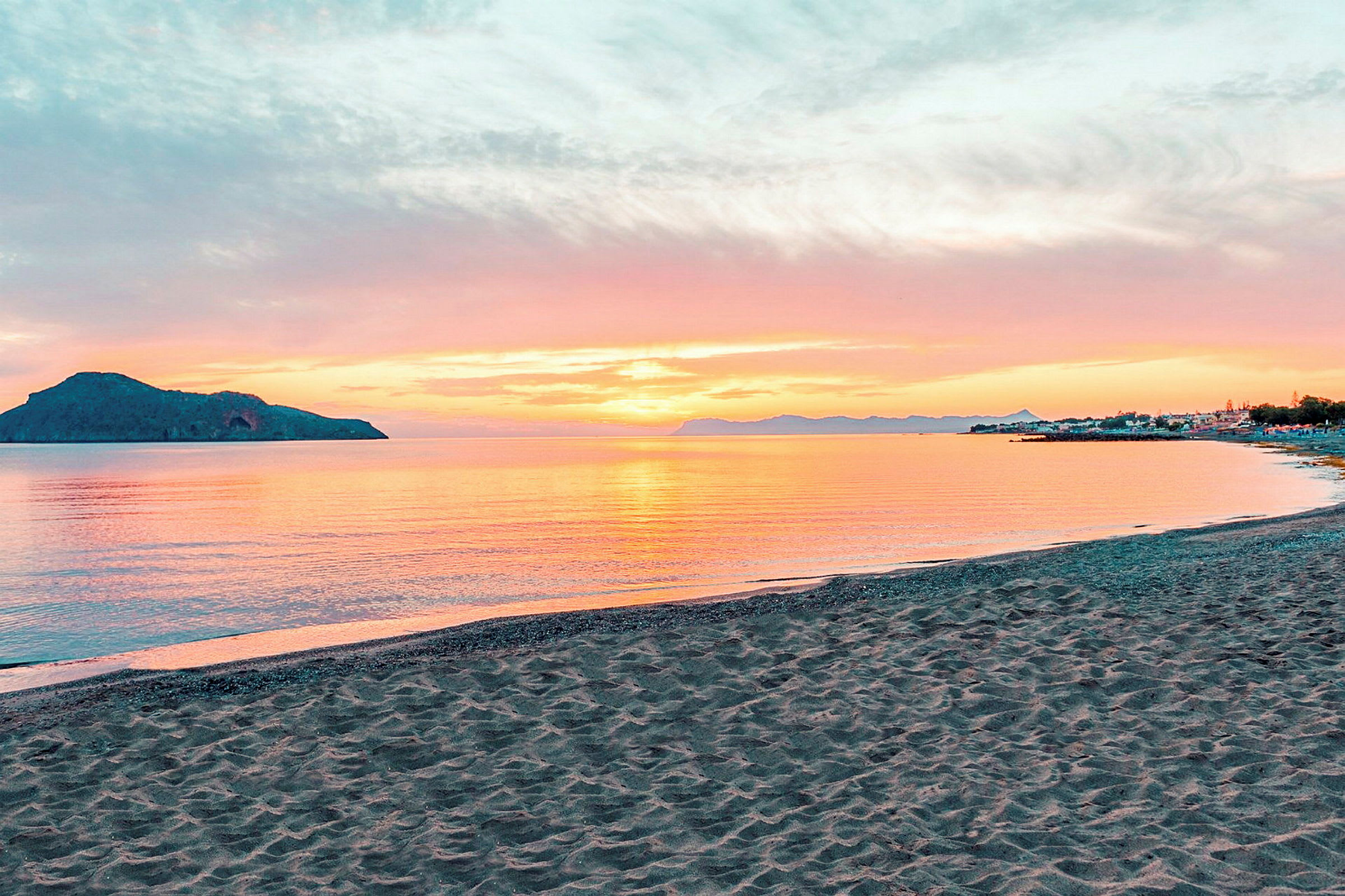 En strand med gyllene sand framför ett stilla vatten vid solnedgången. (AI-genererad text)