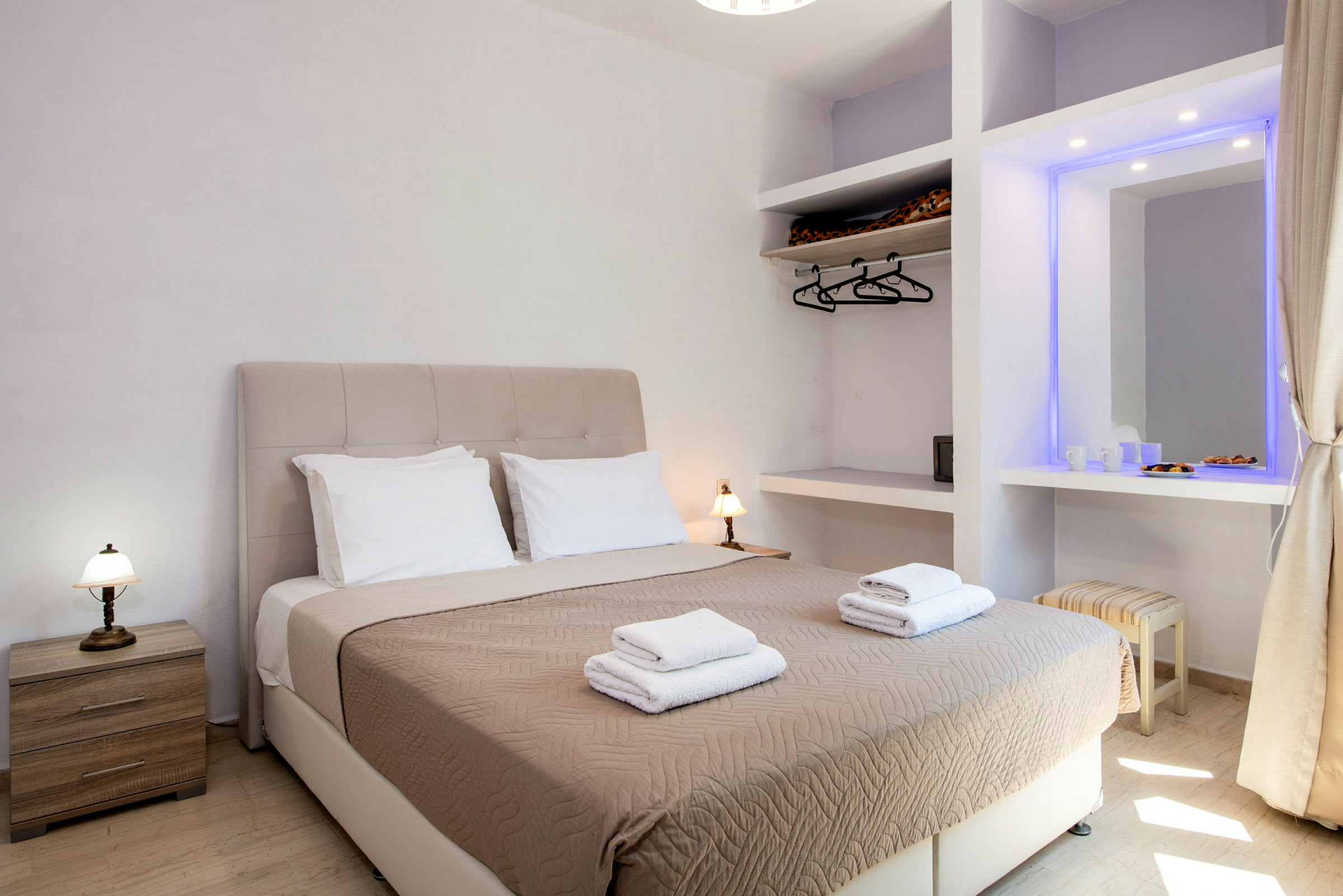Ett hotellrum med en dubbelsäng utrustad med beige sängöverkast och två uppsättningar handdukar, samt sidobord och garderob. (AI-genererad text)