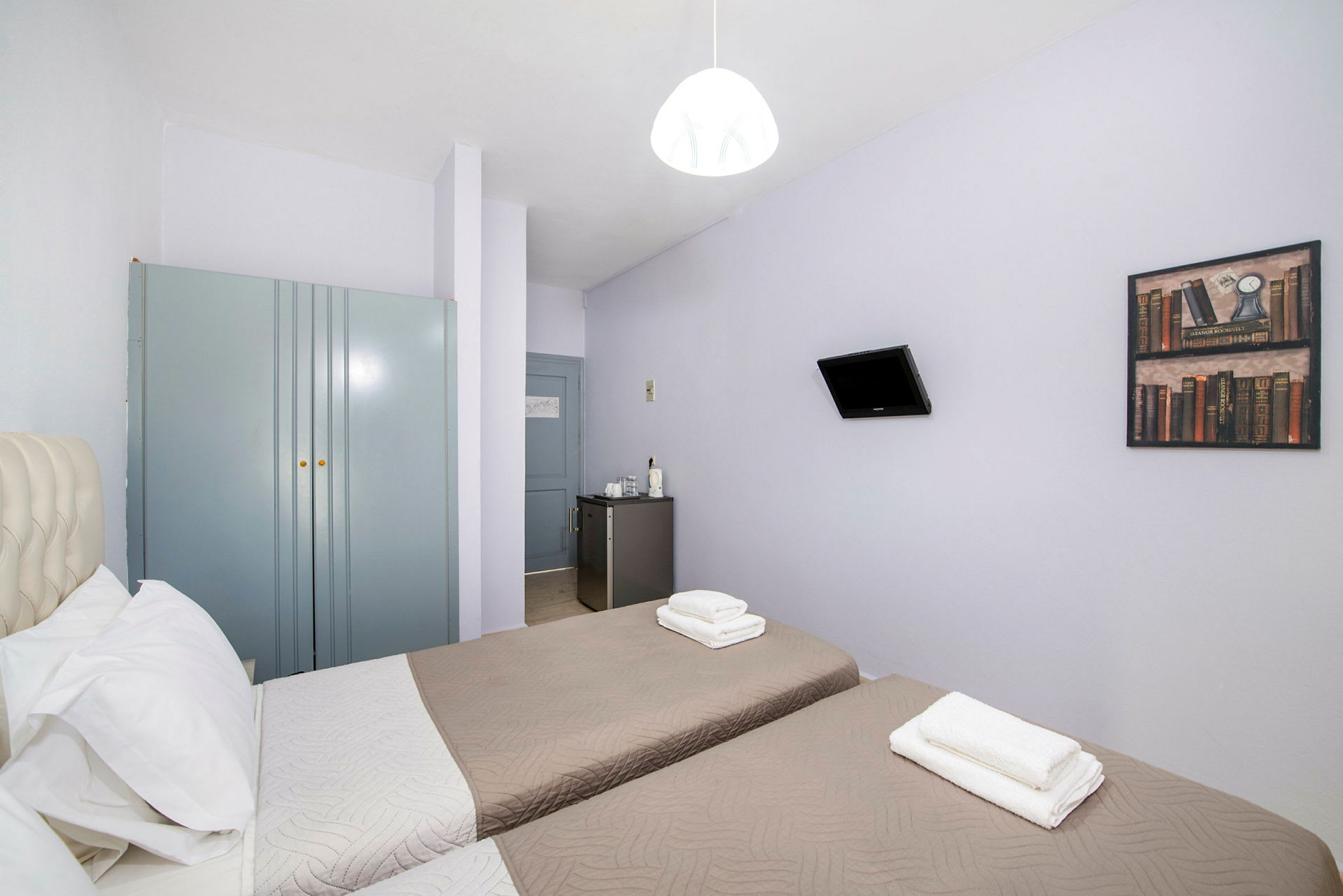 Hotellrum med två enkelsängar, en garderob, en liten kyl och en väggmonterad TV. (AI-genererad text)