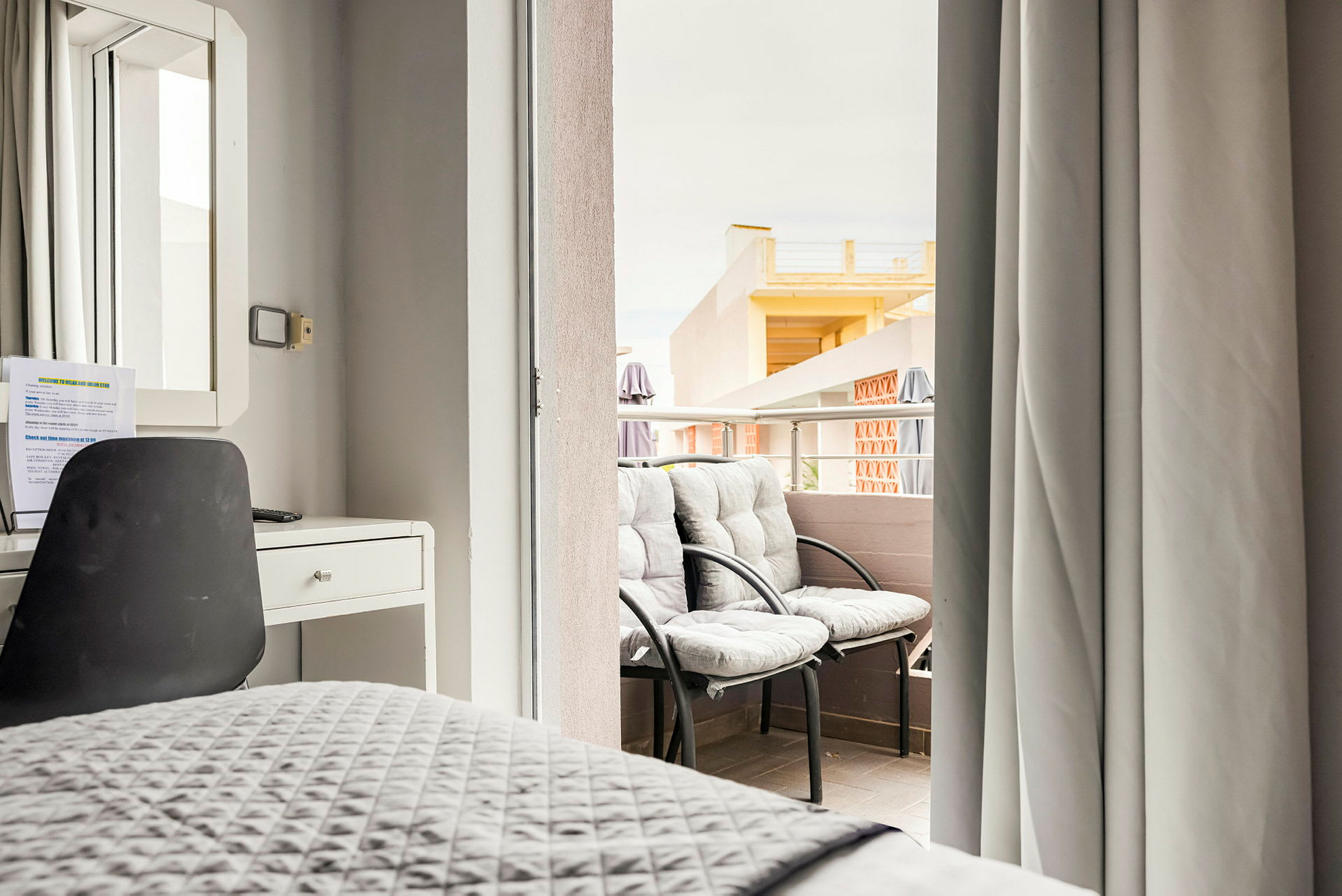 En hotellrumsinredning med skrivbord och stol och utsikt över en balkong med två stolar. (AI-genererad text)