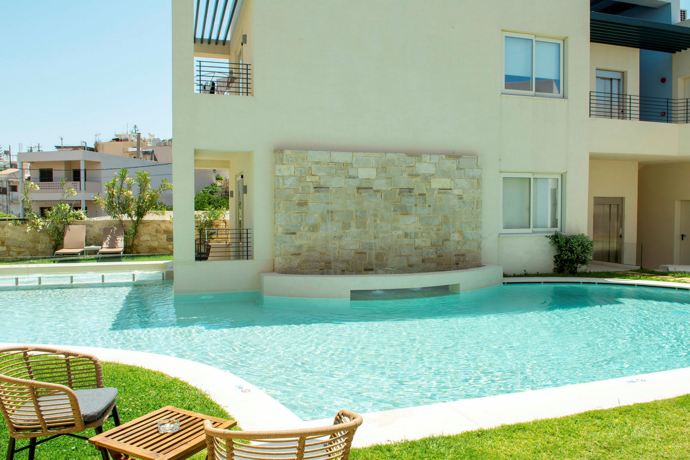 Bild av en utomhuspool vid ett modernt byggnadskomplex med sittmöbler på en gräsmatta. (AI-genererad text)