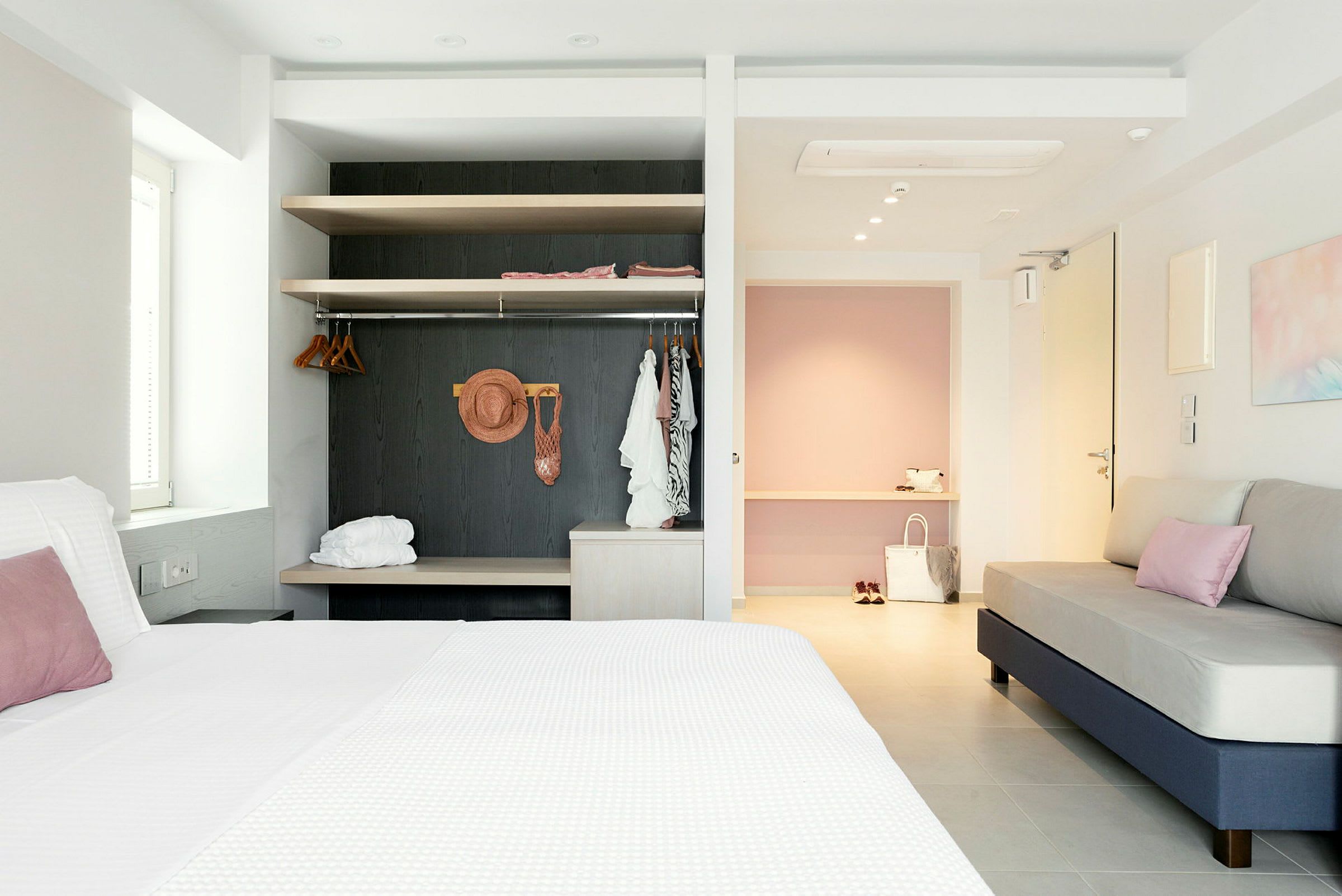 Ett rymligt hotellrum med en säng och ett vardagsområde, innehållande en soffa och en öppen garderob. (AI-genererad text)