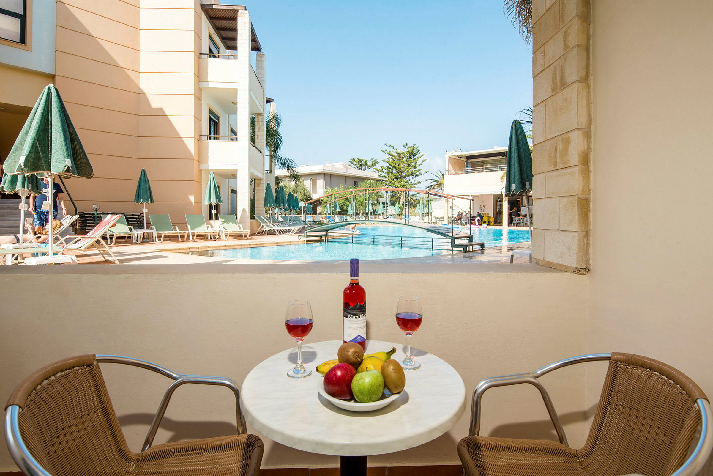 Bilden visar ett bord med frukt och vin framför en swimmingpool och en byggnad. (AI-genererad text)
