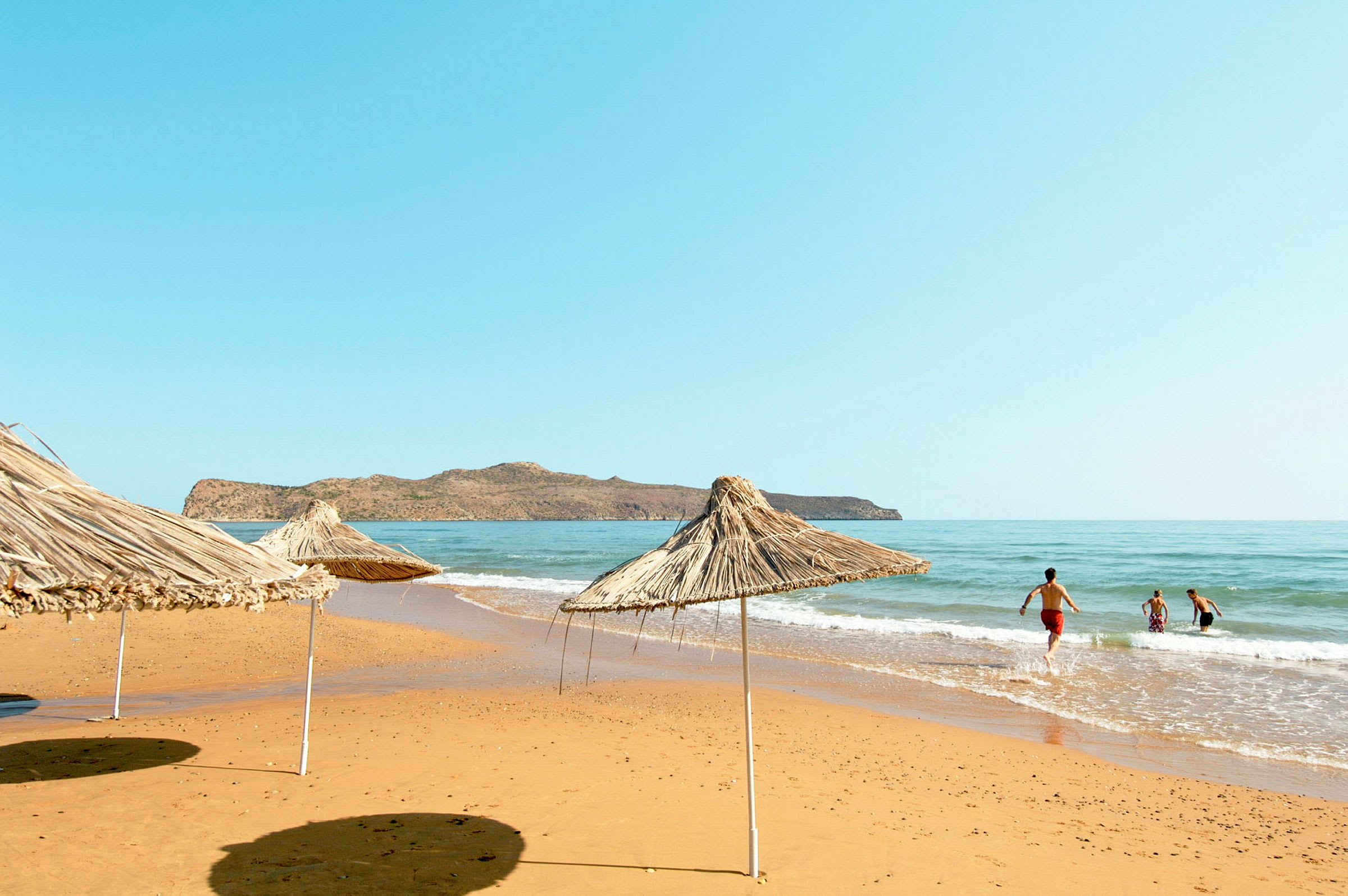 Strand med parasoller av vass samt människor som badar i havet. (AI-genererad text)