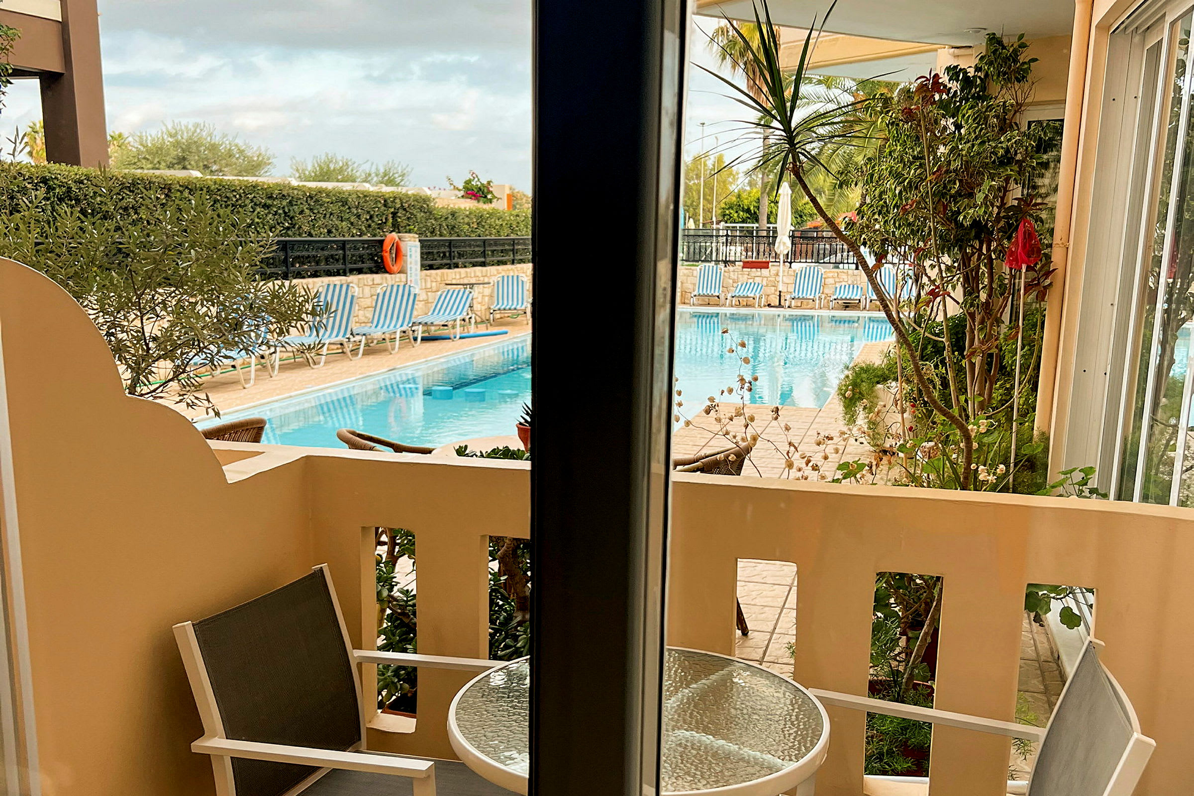 Utsikt från en balkong mot en pool med solstolar. (AI-genererad text)