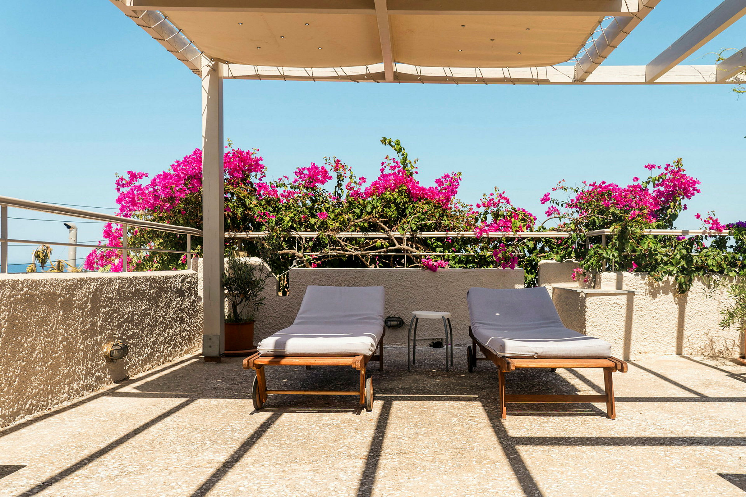 Terrass med två solstolar, bougainvillea och takavsats under blå himmel. (AI-genererad text)