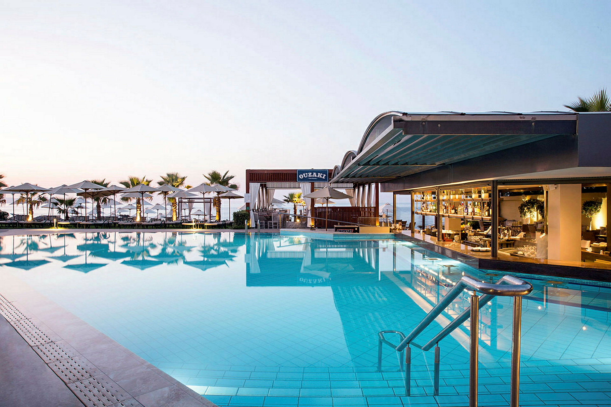 En stor pool vid en hotellrestaurang med utsikt över havet. Solstolar och parasoller omger området. (AI-genererad text)