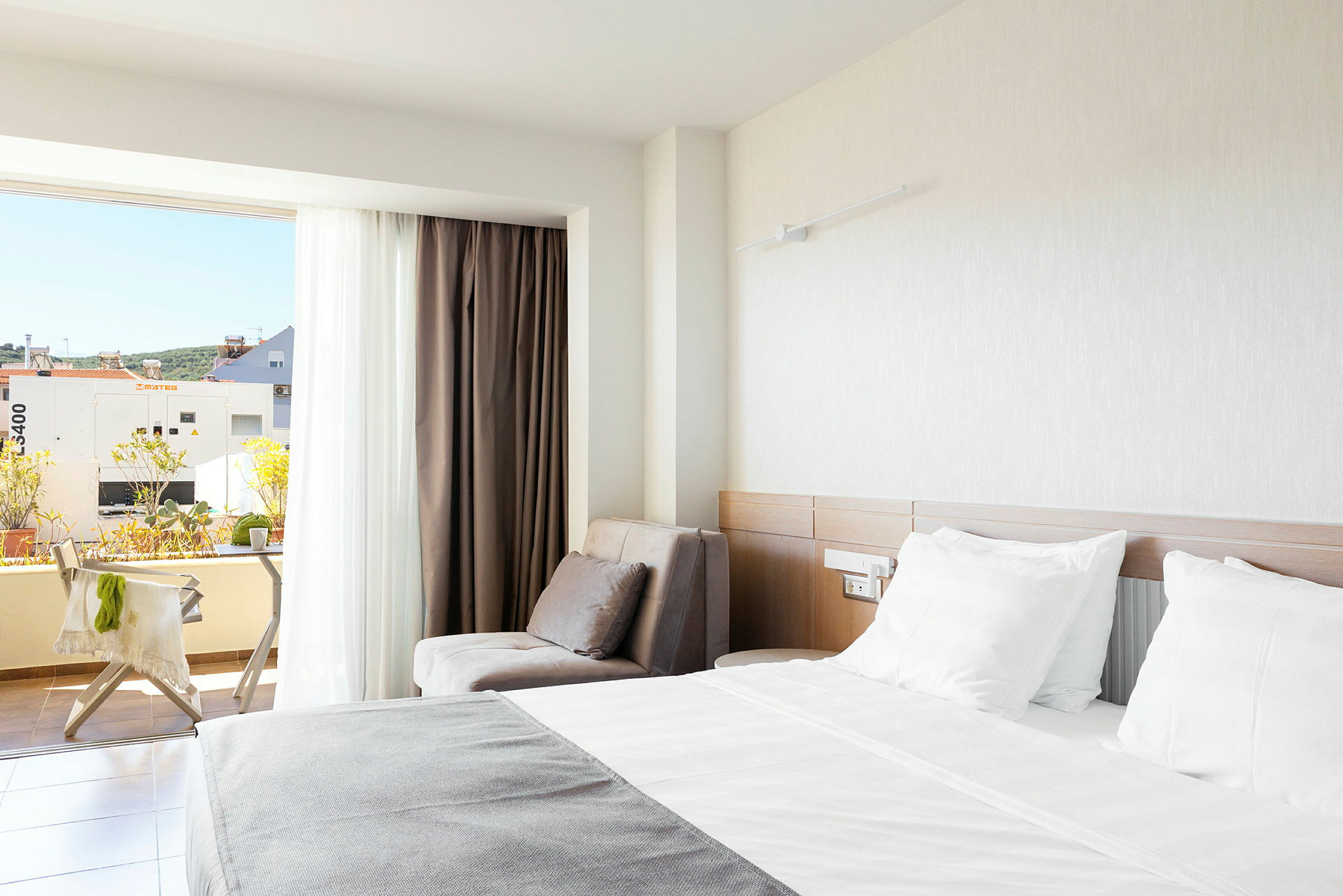 Ett hotellrum med en dubbelsäng, en fåtölj och en balkong med utsikt. (AI-genererad text)