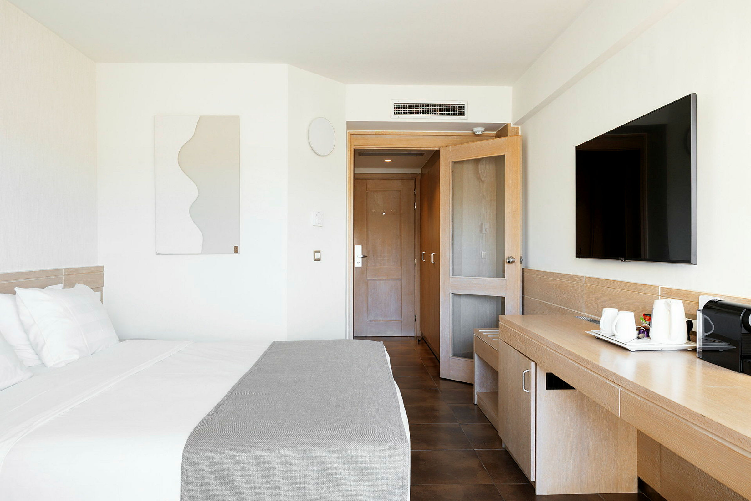 Ett modernt hotellrum med en säng, ett skrivbord, en TV och en dörr i bakgrunden. (AI-genererad text)