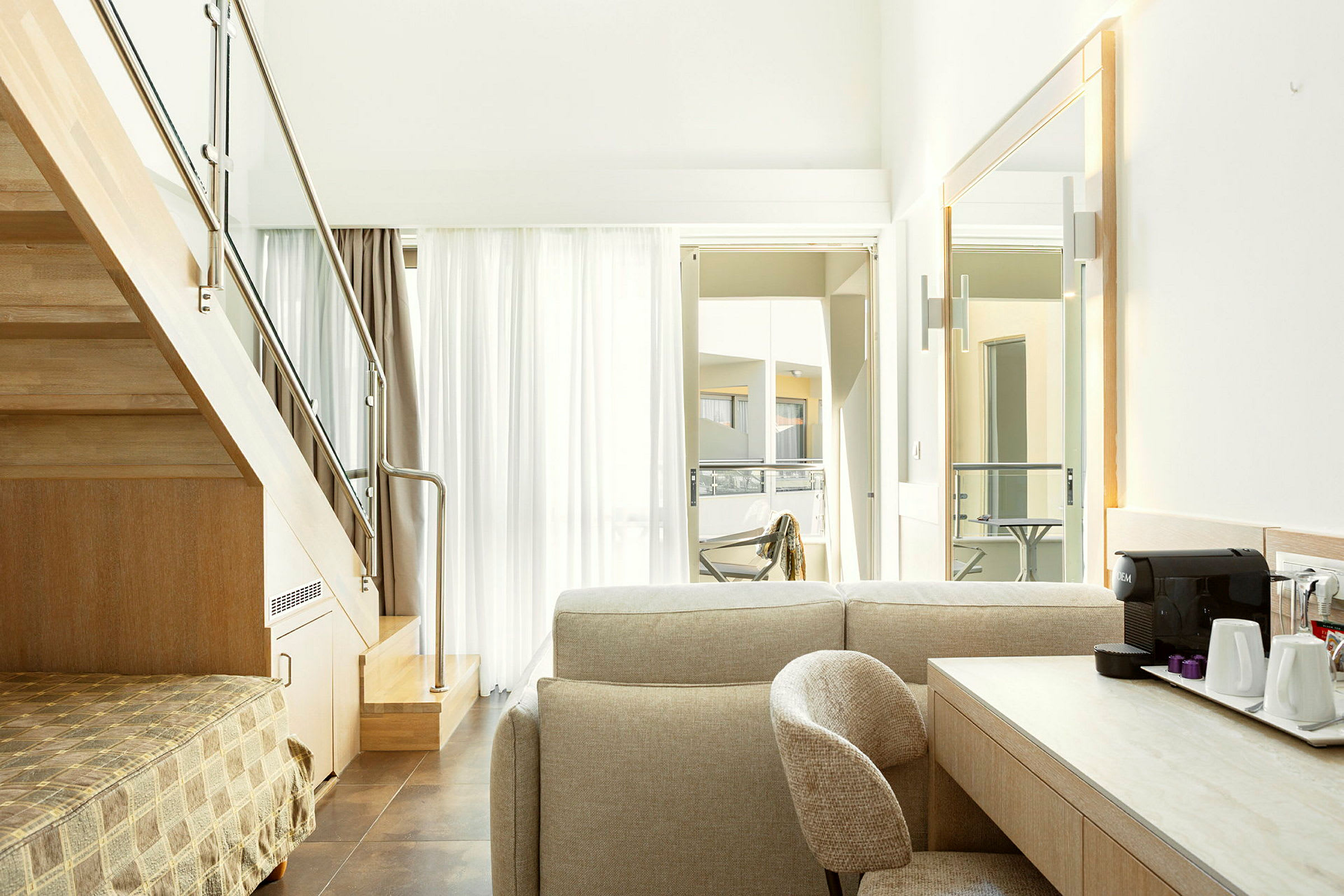 Interiörbild av ett modernt hotellrum med en trappa, sittgrupp och ett skrivbord med kaffemaskin. (AI-genererad text)