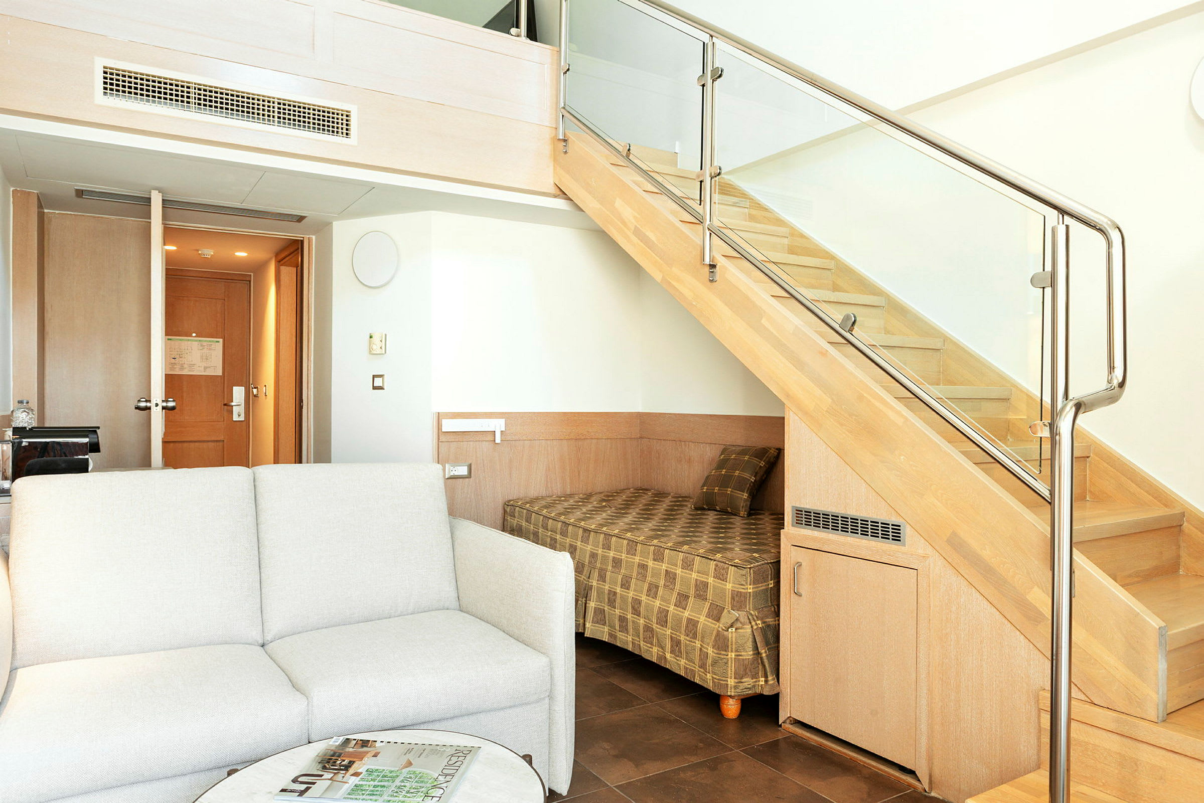 Ett hotellrum med en soffa, ett bord och en våningssäng under en trappa. (AI-genererad text)