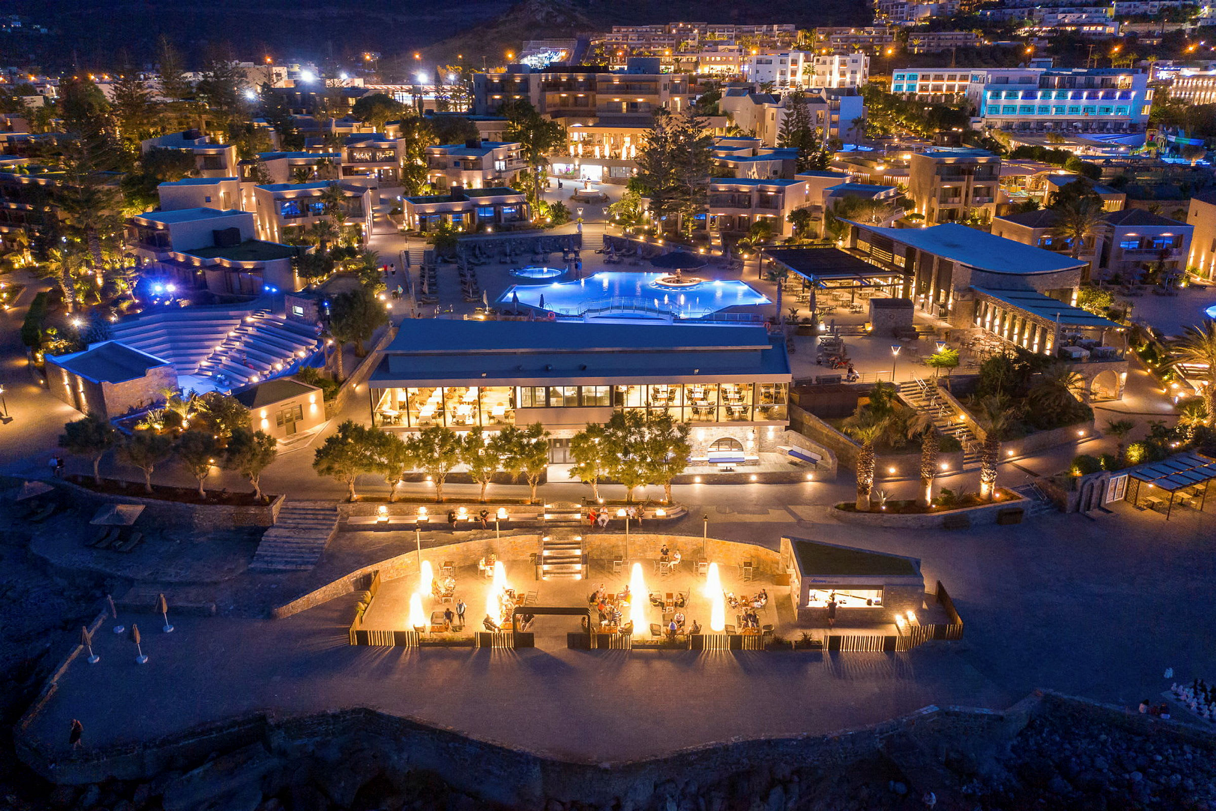 En resort med flera byggnader, pooler och utomhusområden upplysta på kvällen. (AI-genererad text)