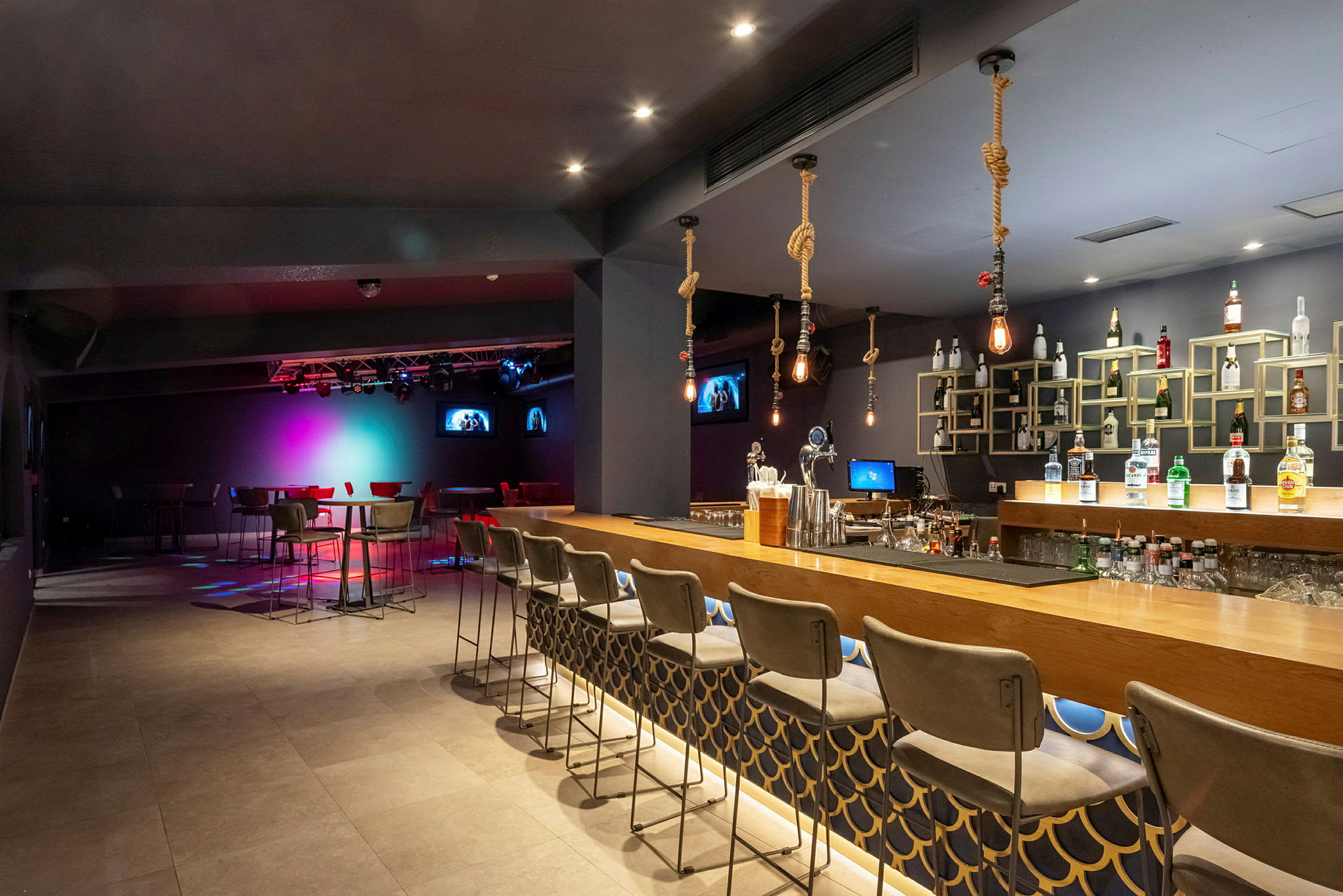 Inomhusbild av en bar med sittplatser och en upplyst scen i bakgrunden. (AI-genererad text)
