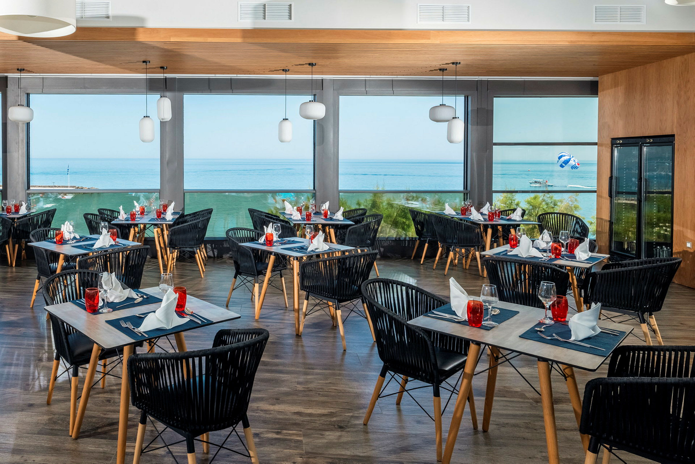 En restaurang med dukade bord och utsikt över havet genom stora fönster. (AI-genererad text)