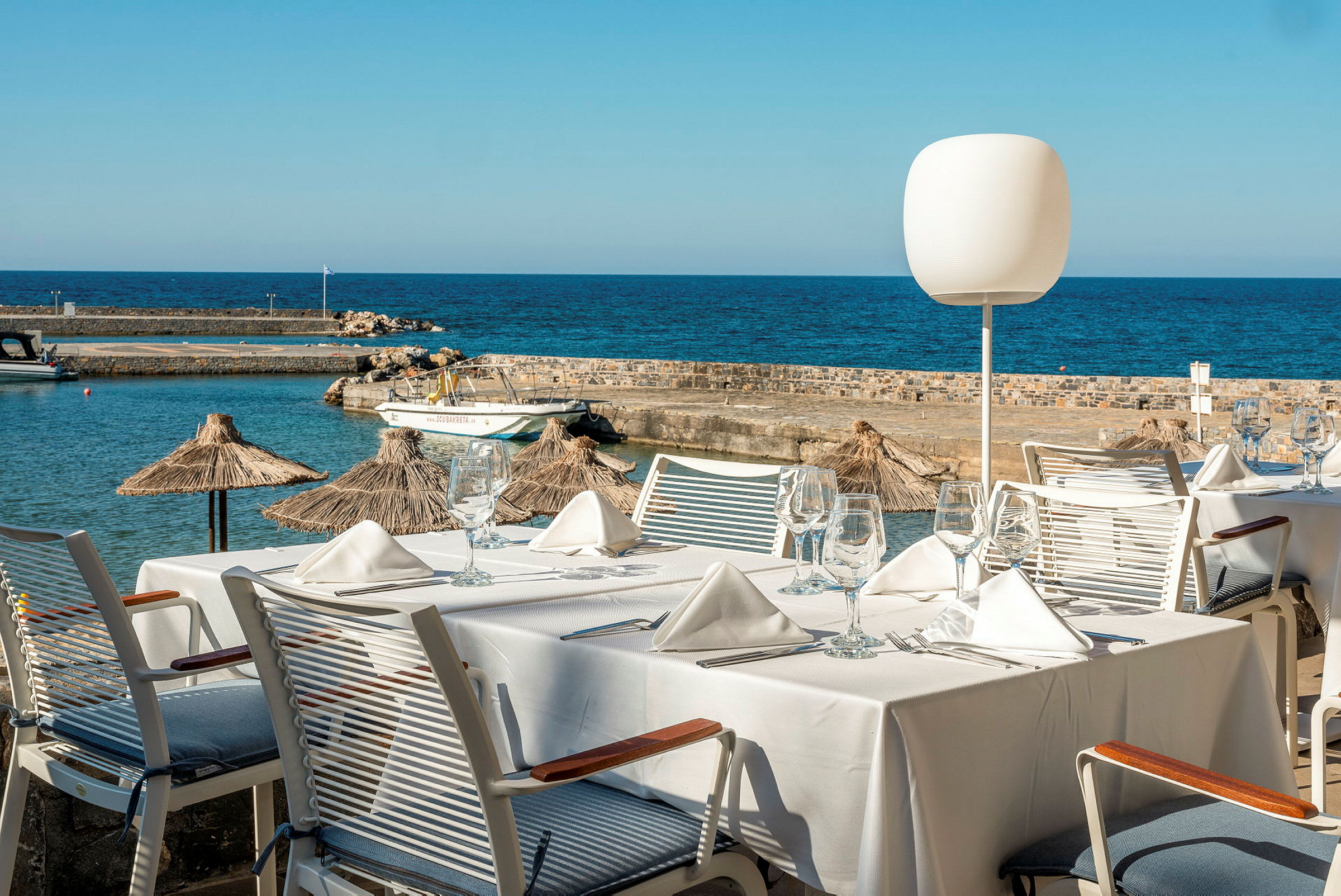 Ett dukat bord med vita servetter och glas, med utsikt över havet och en brygga. (AI-genererad text)