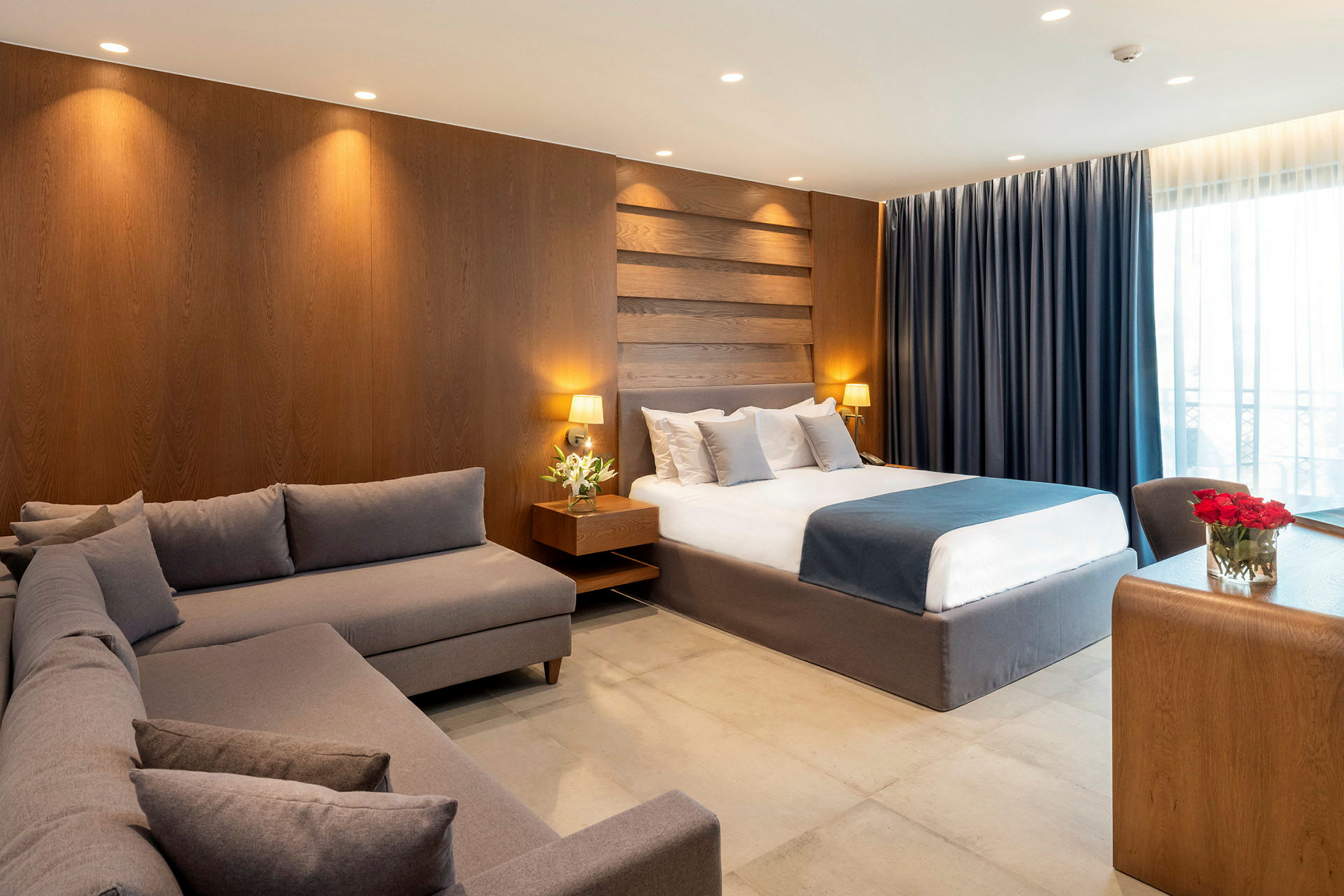 Ett hotellrum med en stor säng, en grå soffa och ett träskrivbord. (AI-genererad text)