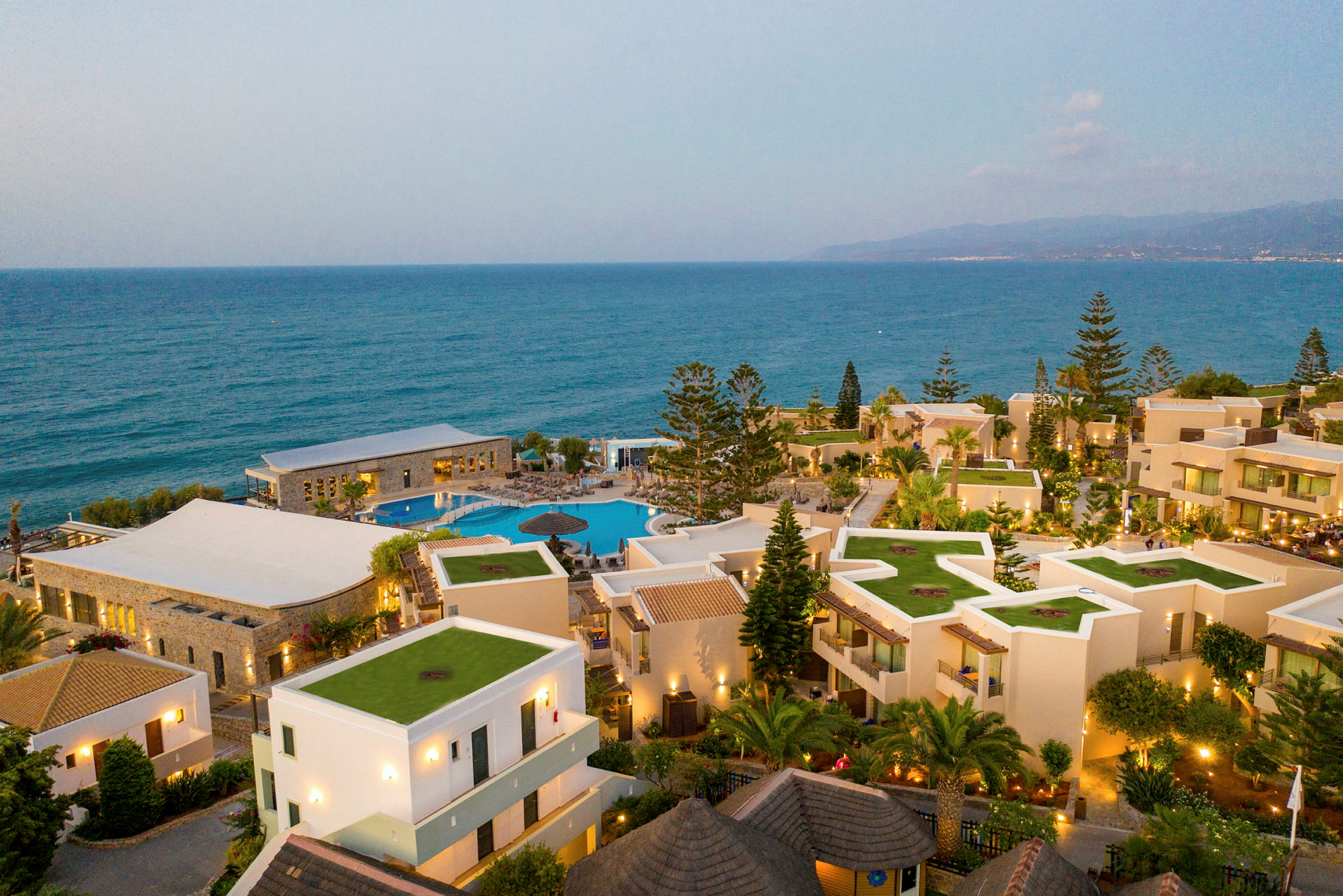 Bild av ett hotellområde vid havet med pool och gröna tak på byggnader. (AI-genererad text)