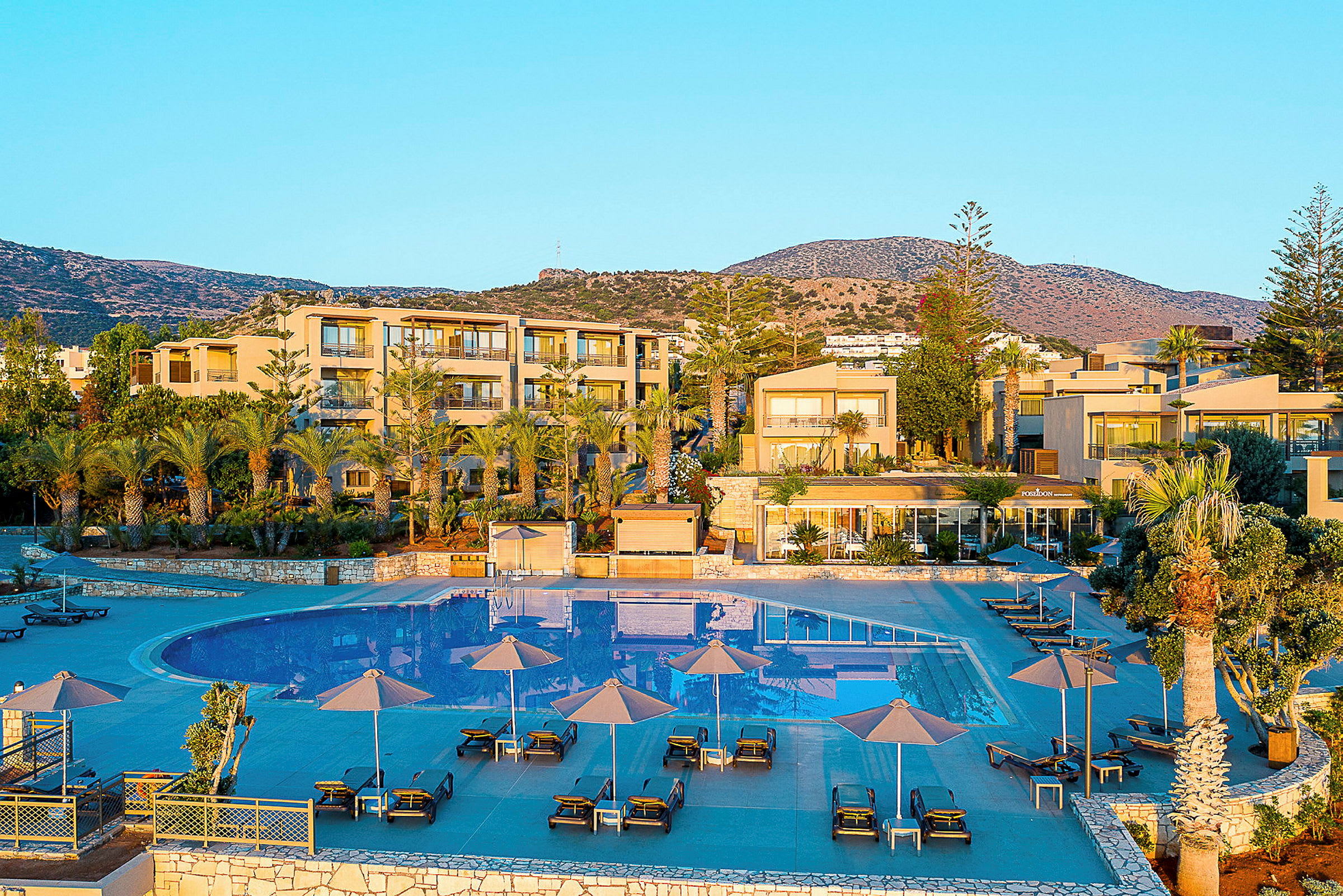 Bild på en resort med pool och omgivande byggnader mot en bergsklippa. (AI-genererad text)