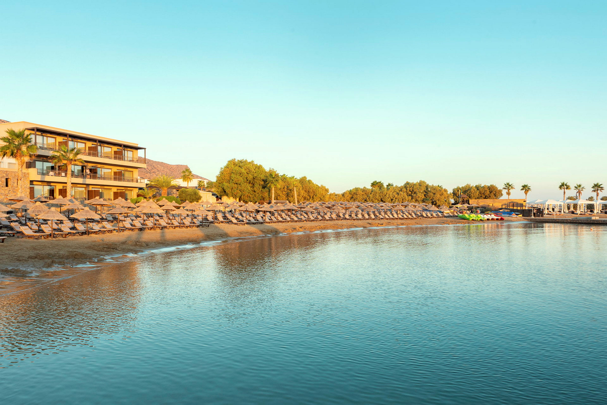 En strand med solstolar och parasoller vid ett hotell med utsikt över lugnt vatten. (AI-genererad text)