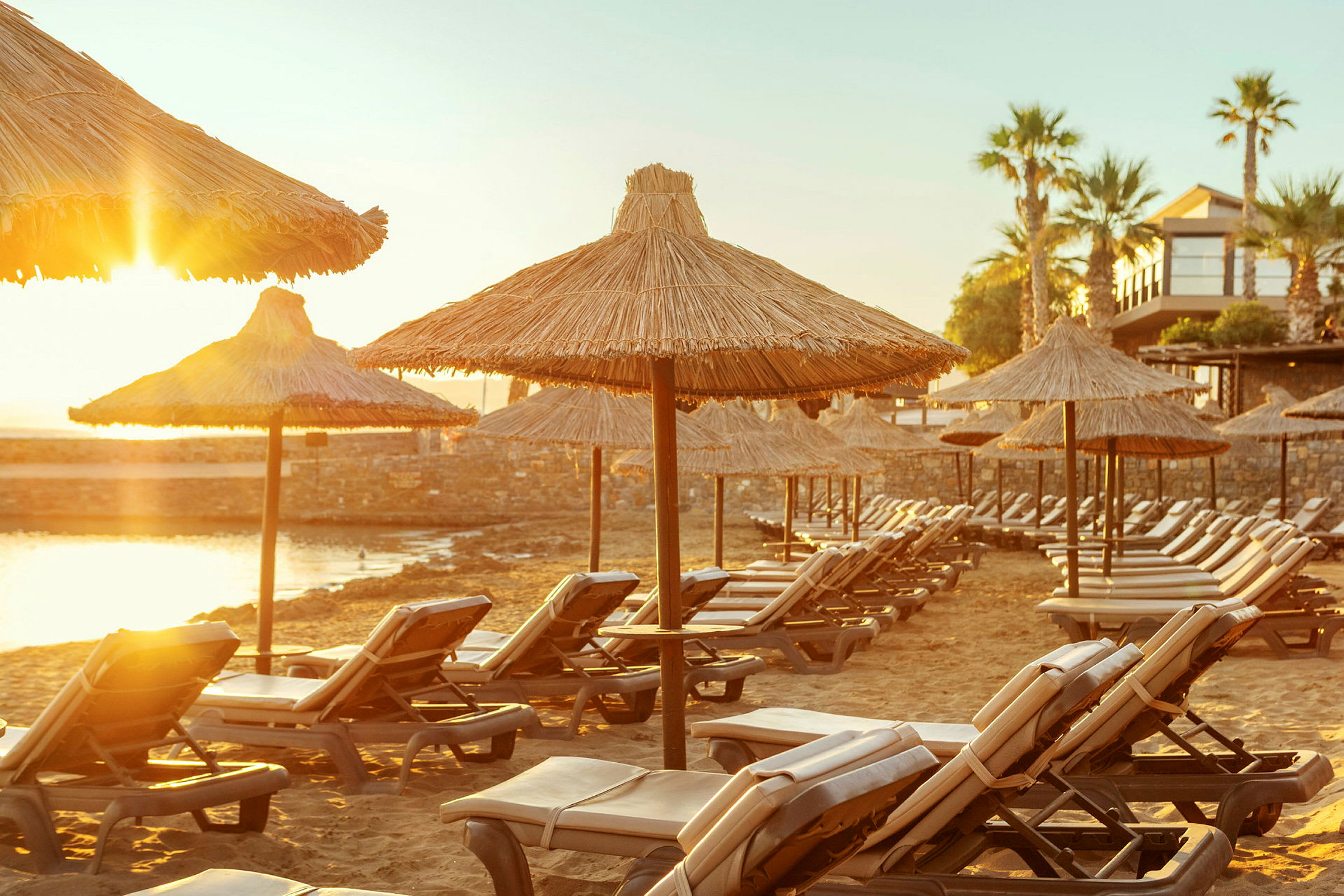 En strand med solstolar och halmtak, upplyst av kvällssol. (AI-genererad text)