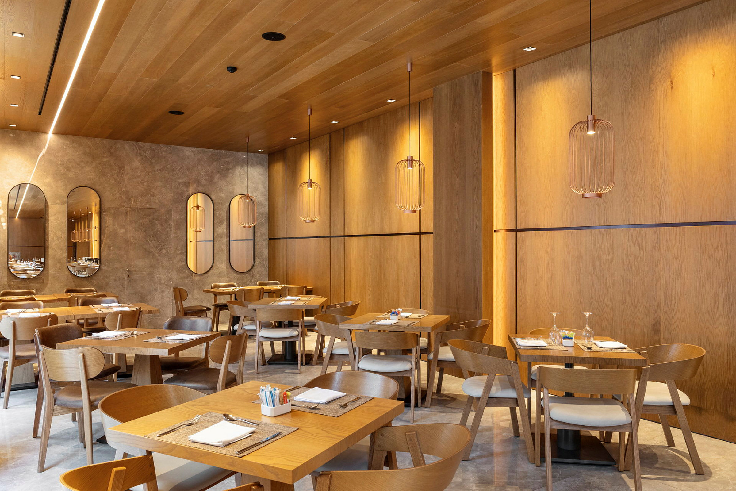 En modern restaurang med träpaneler på väggar och tak, eleganta hängande lampor och dukade bord med trästolar. (AI-genererad text)