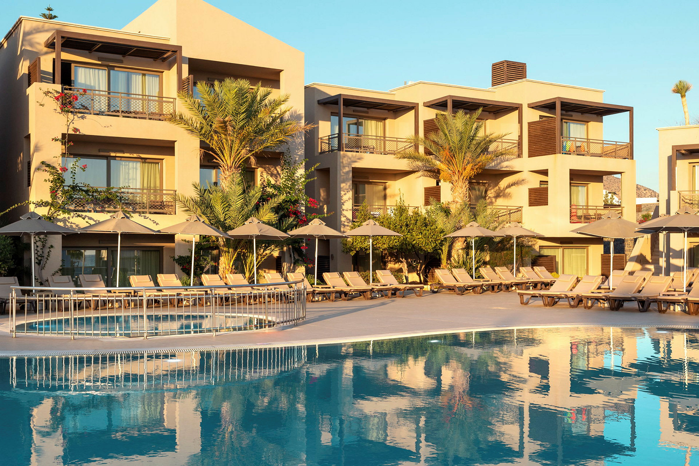 Bild av ett hotell med flera våningar, en pool framför och solstolar med parasoller. (AI-genererad text)